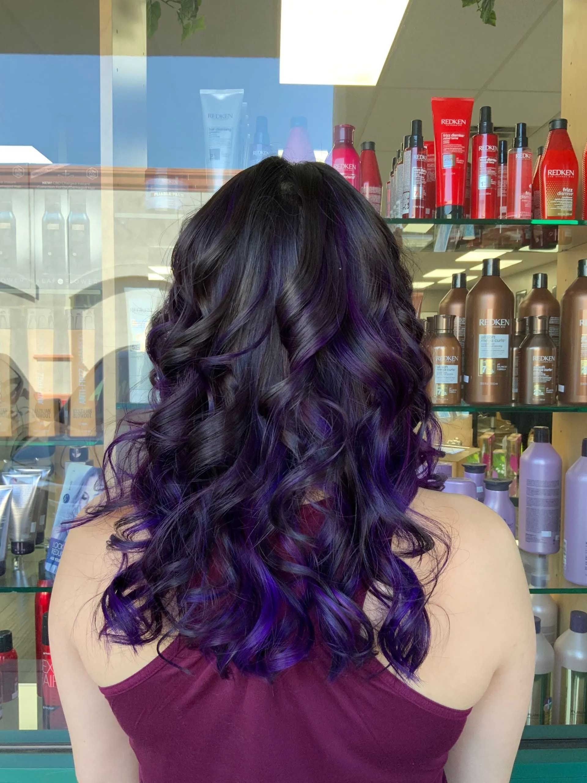 Woman with wavy black hair transitioning to vibrant purple at the ends, salon setting.