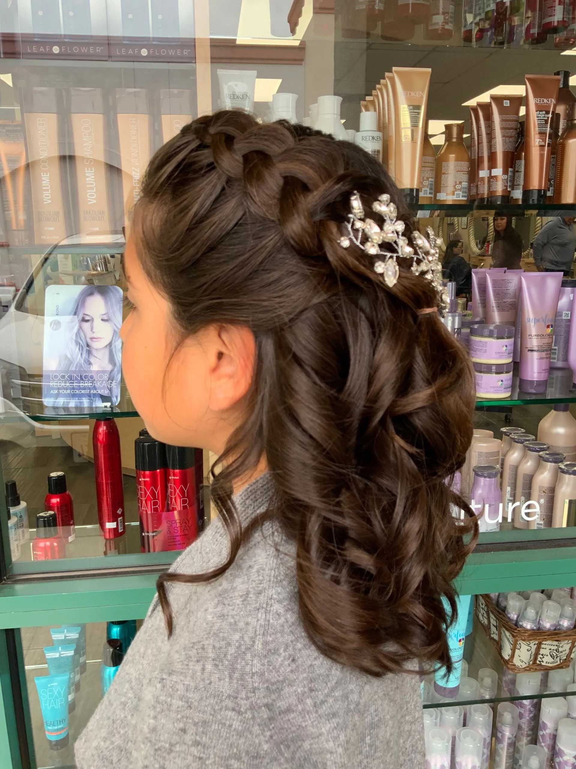 Young person with brown curly hair, side braid, and decorative hairpiece, in a salon.