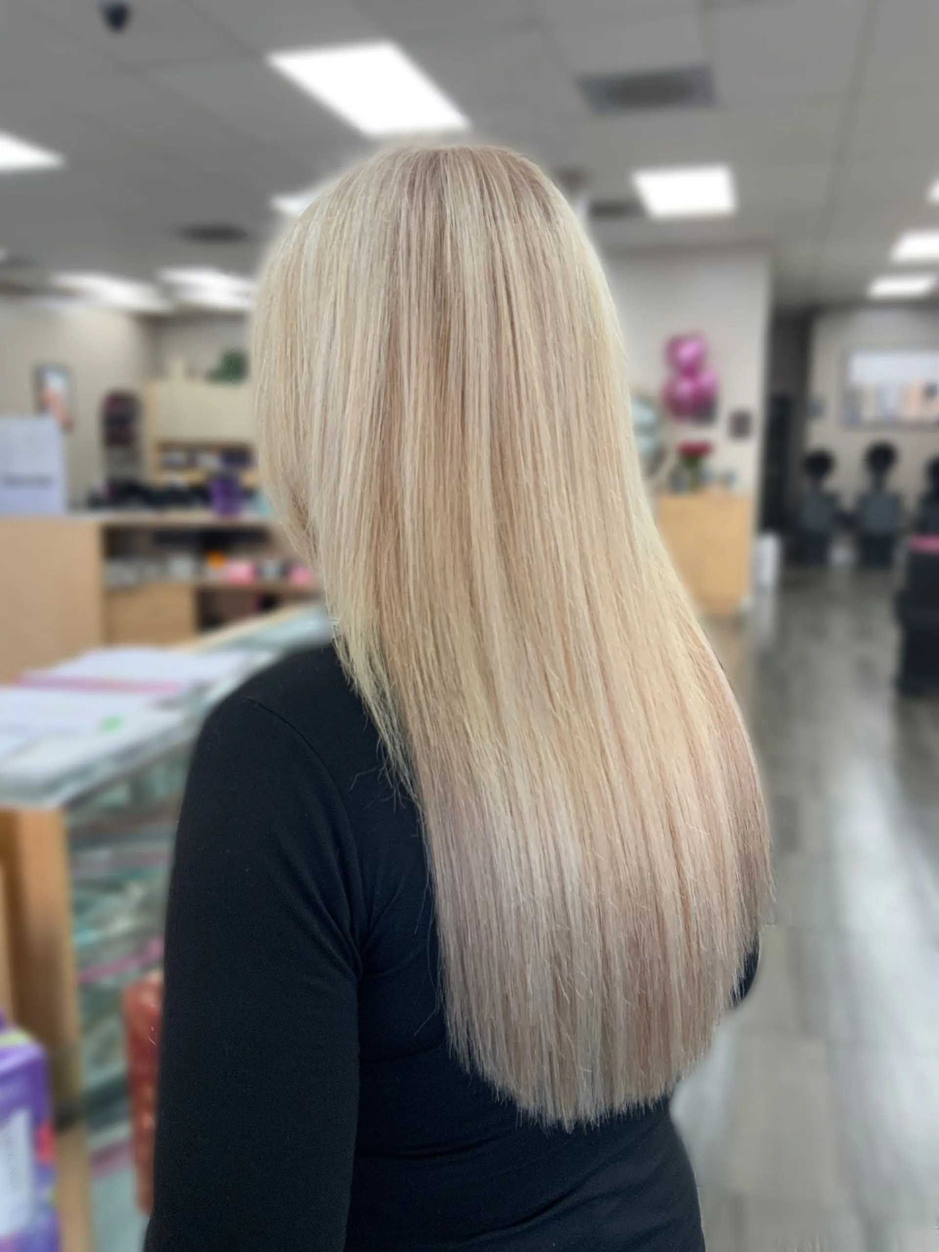 Blonde hair with a crimped texture, styled long. Person's back faces a brightly lit shop interior.
