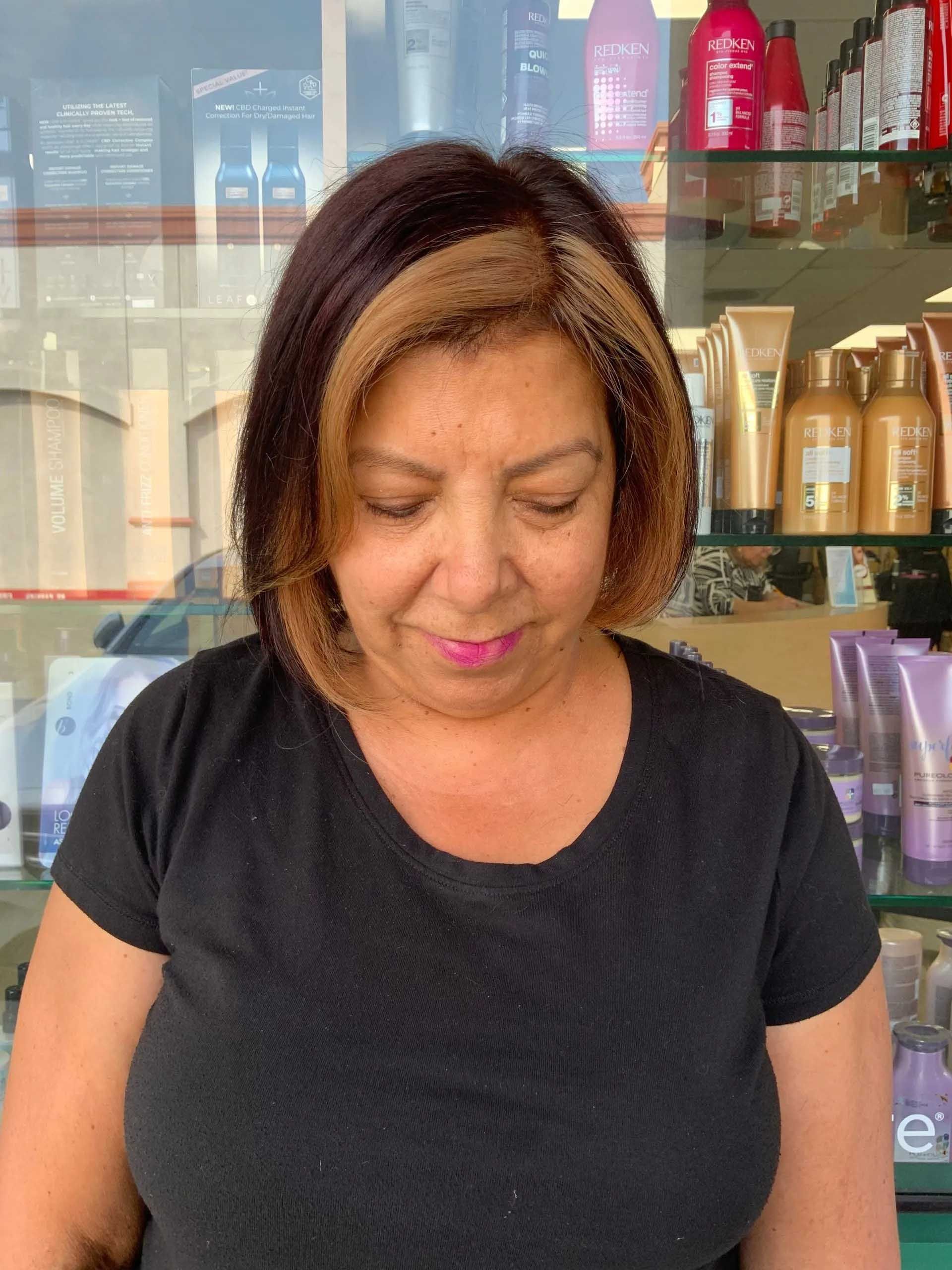 Woman with dark hair and blonde highlights at a salon, looking down.