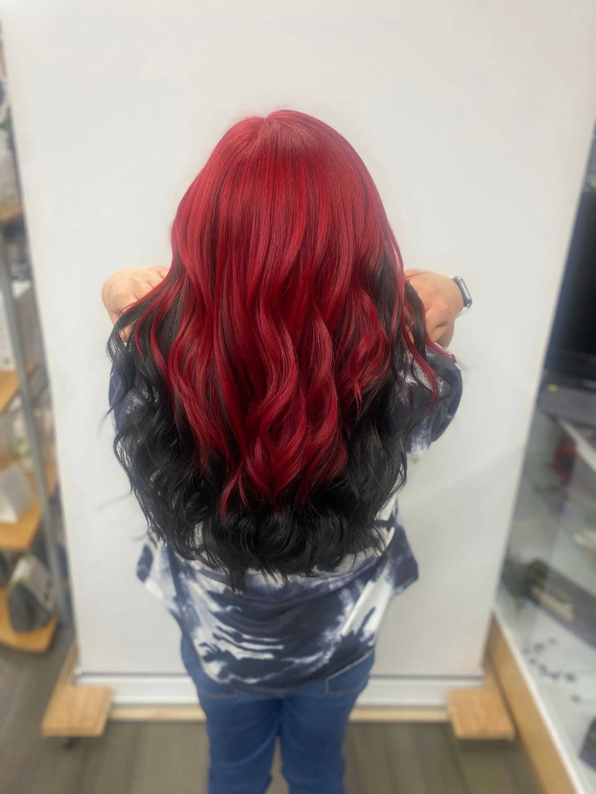 Woman with long, wavy hair; red at top, transitioning to black. Wearing blue jeans and a tie-dye shirt.