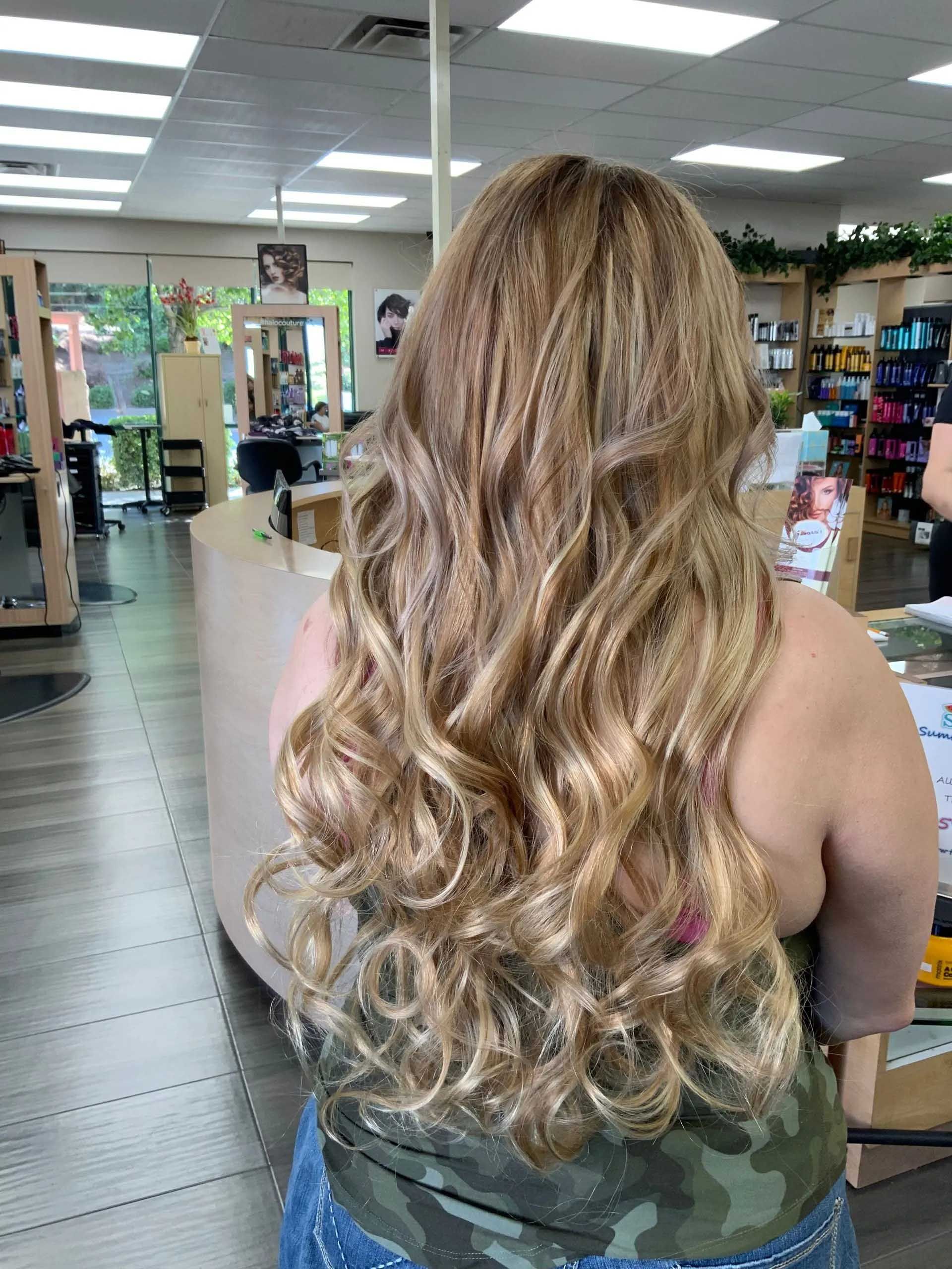 Woman with long, wavy blonde hair in a salon, wearing a camouflage tank top.