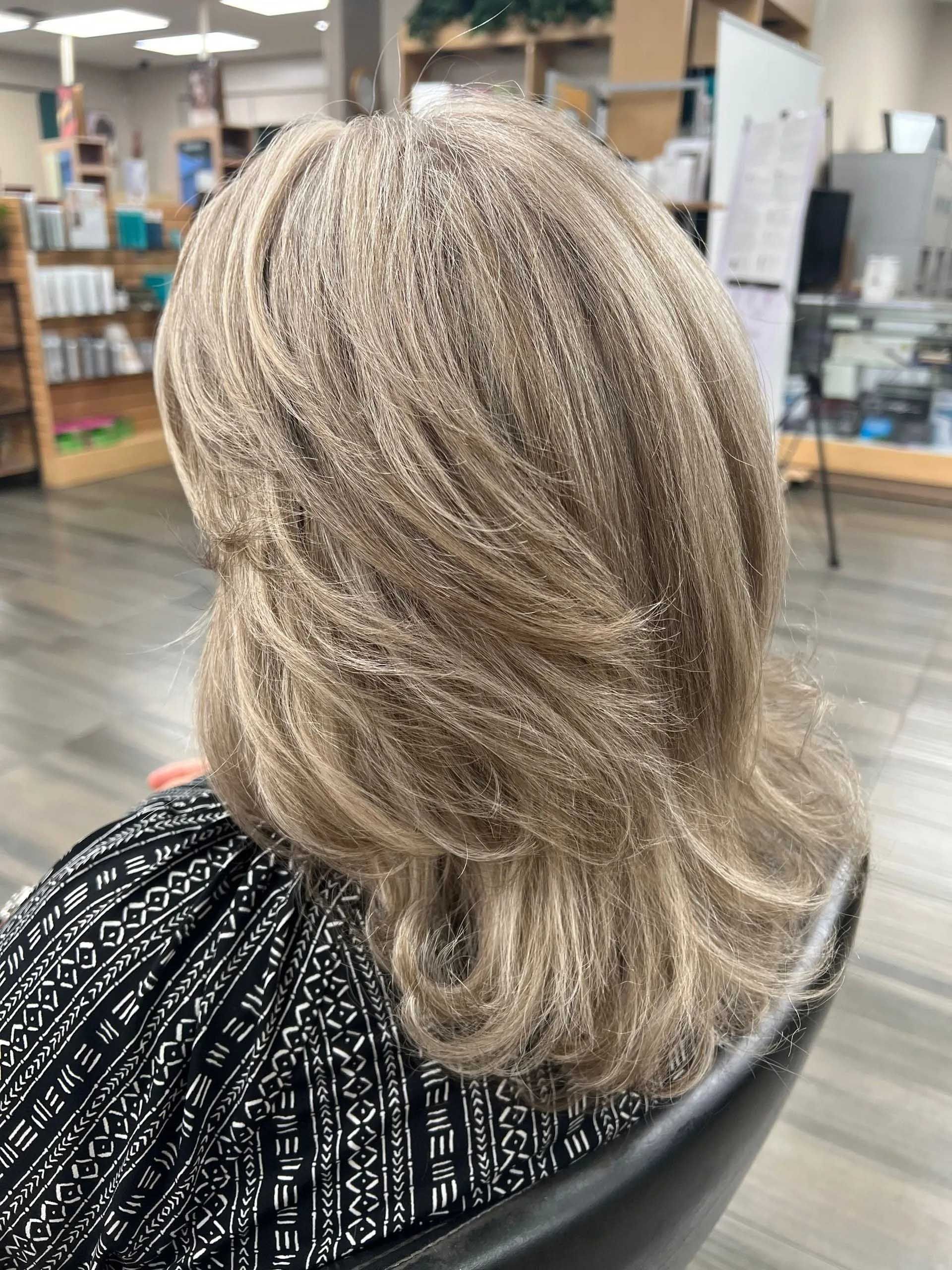 Woman with layered, light brown hair sits in salon chair.