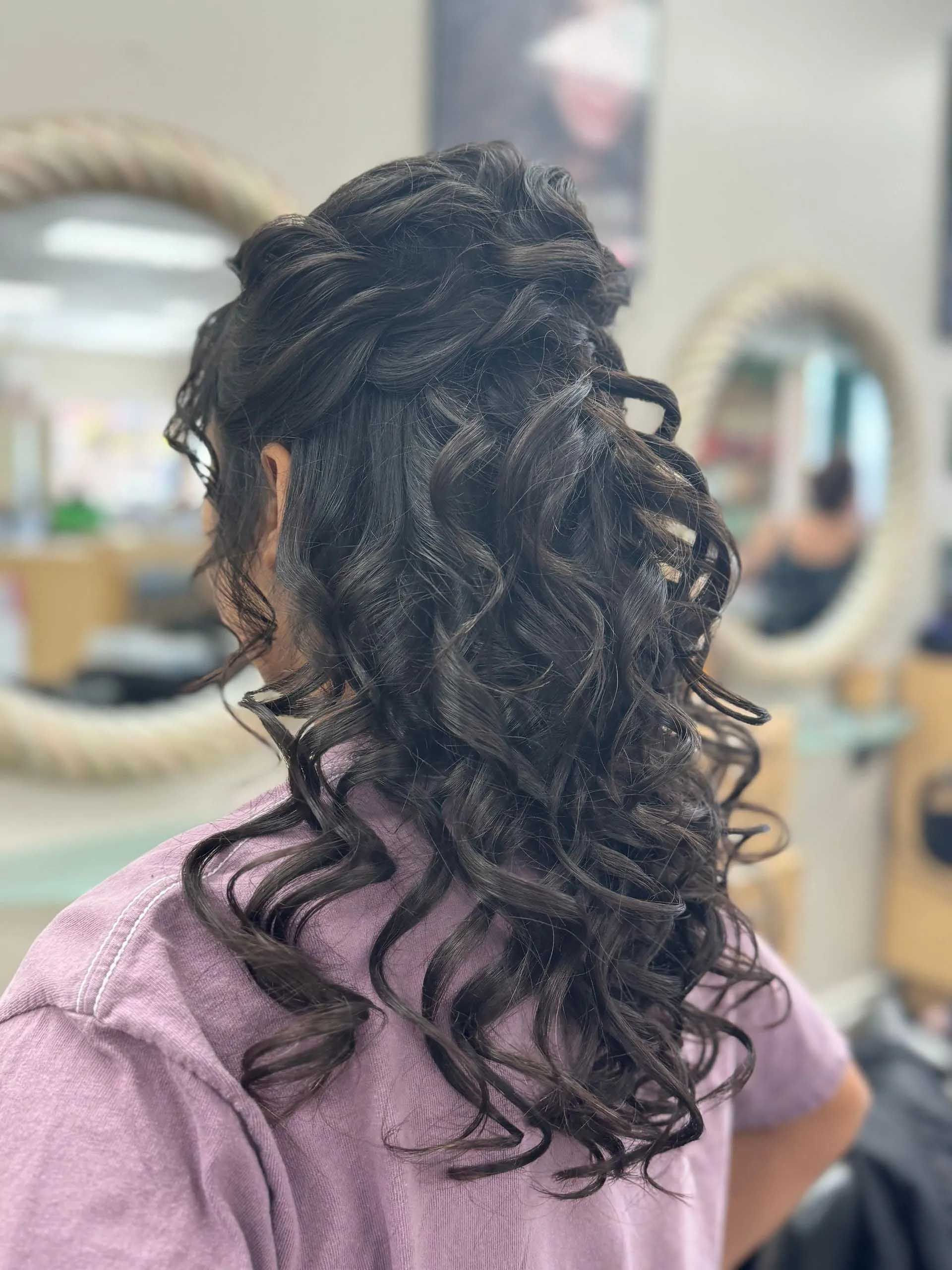 Woman with dark hair styled in an updo with long curls; in a salon setting.