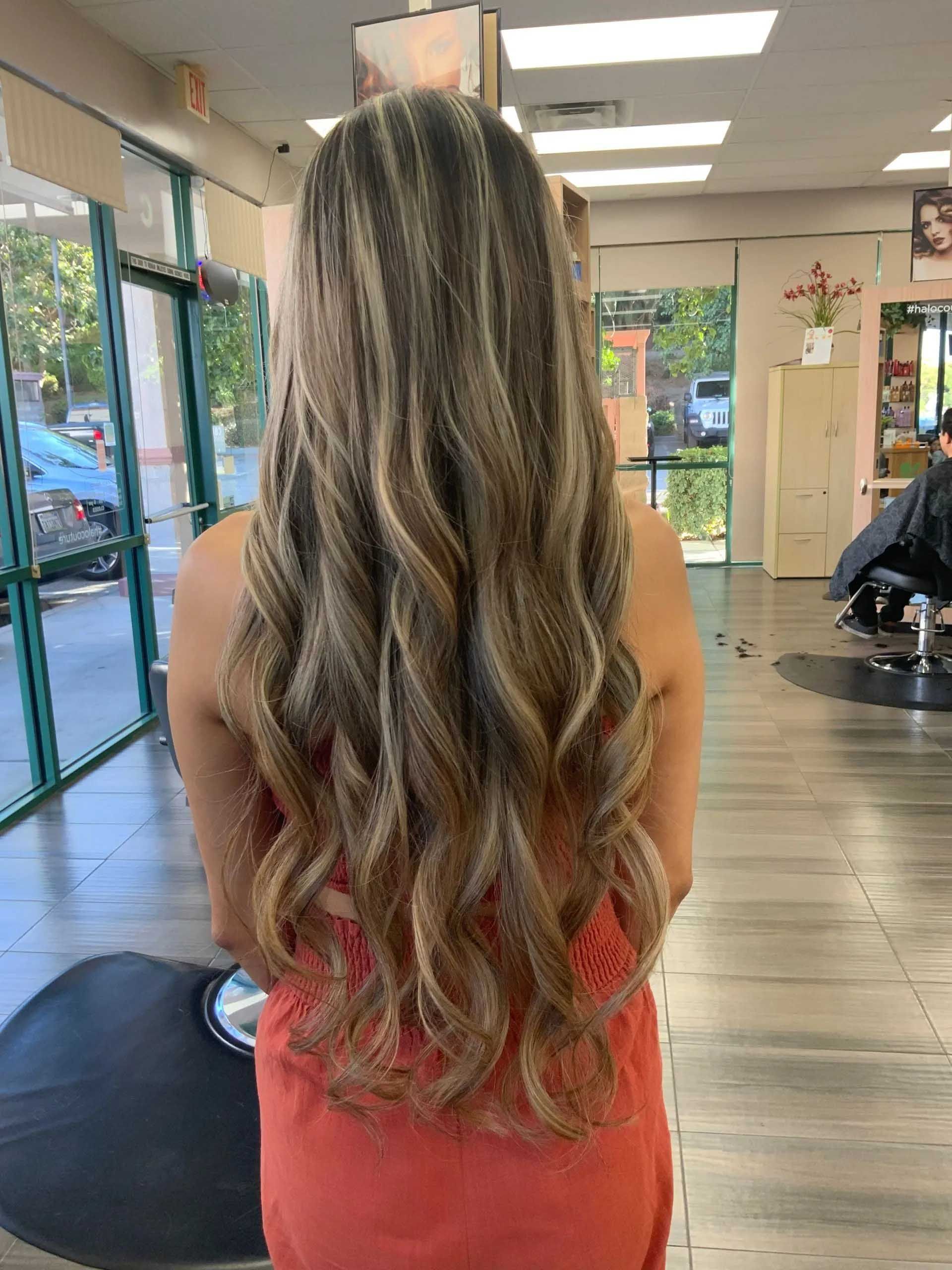 Woman with long, wavy blonde and brown hair stands in a hair salon.
