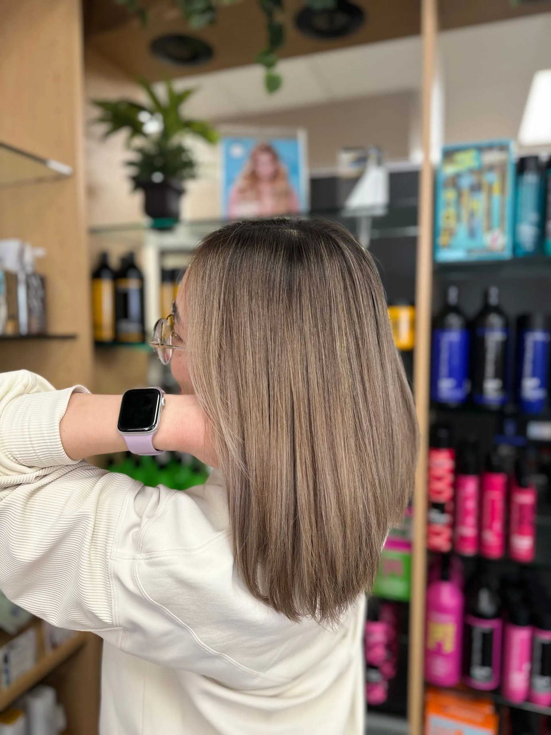 Woman with crimped, blonde hair, holding her neck. Hair products on shelves in background.