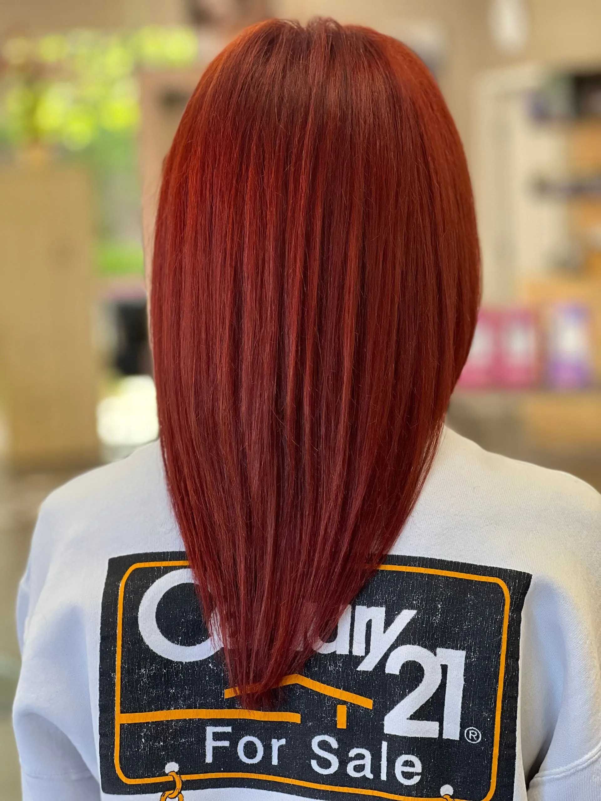 Person with red hair, wearing a white sweater with a Century 21 logo, back view.
