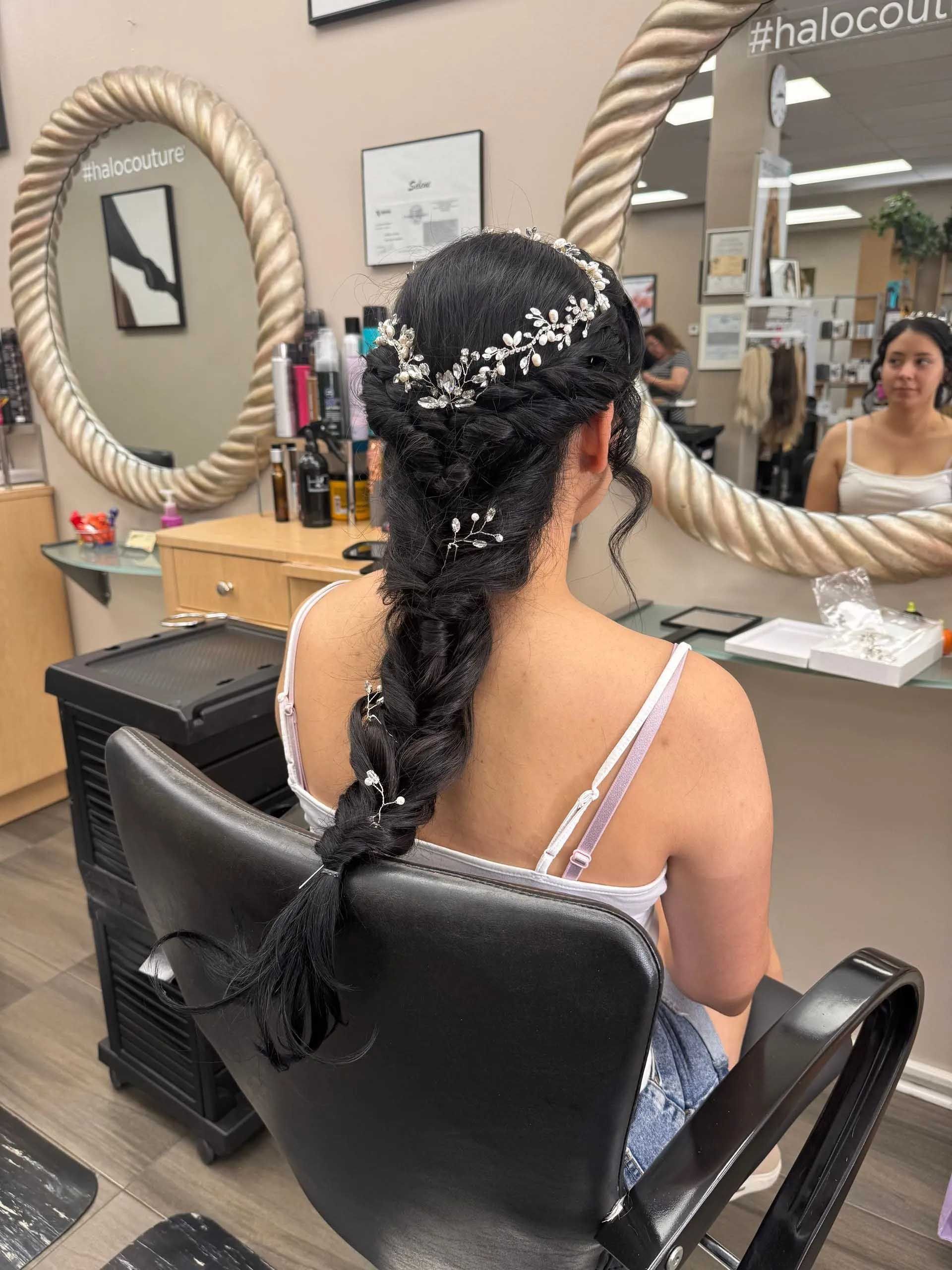 Woman with braided hairstyle adorned with decorative elements, seated in a salon chair.