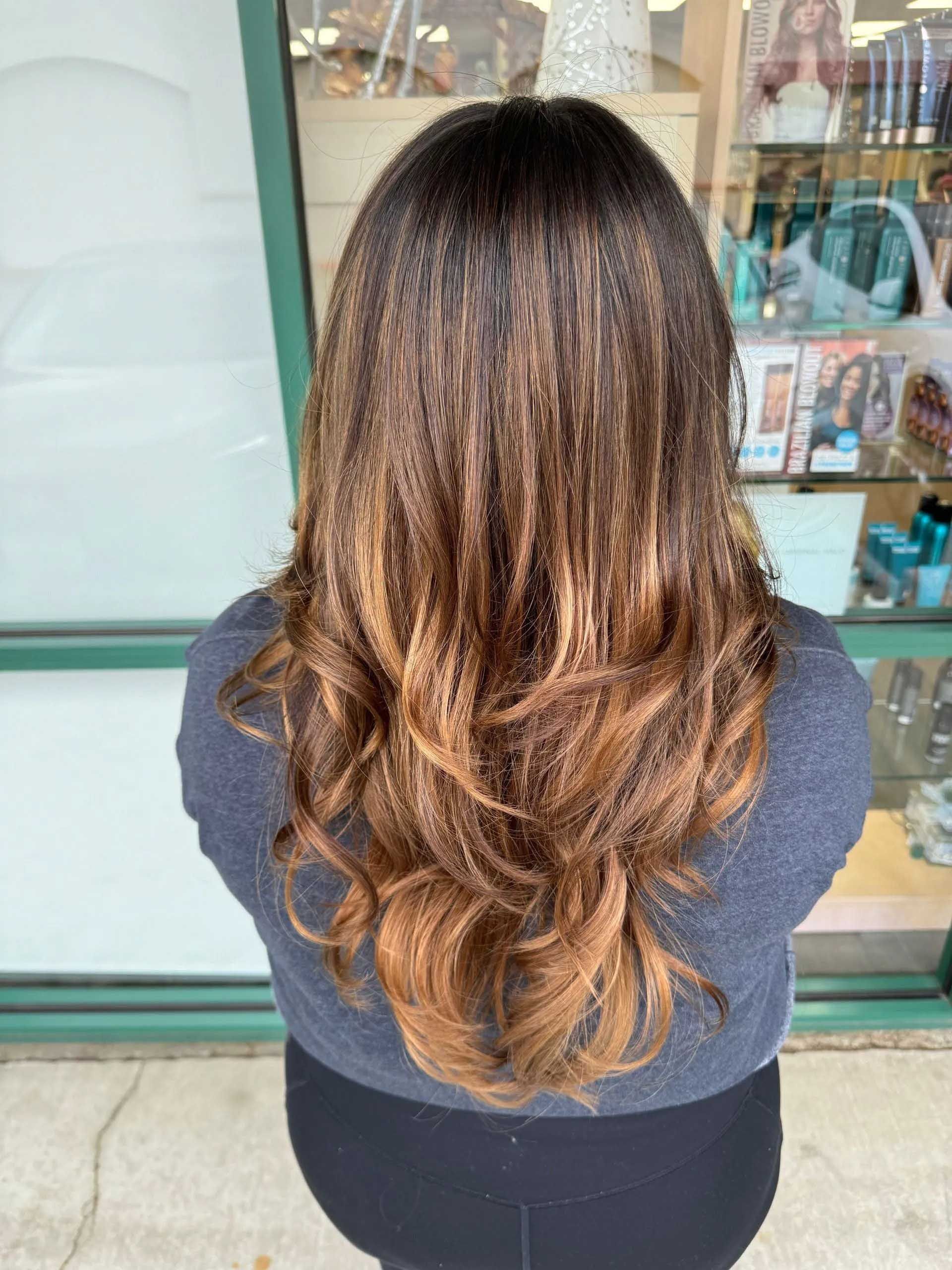 Woman with brown hair, dark at the roots, fading to a warm, lighter brown at the ends, wavy.