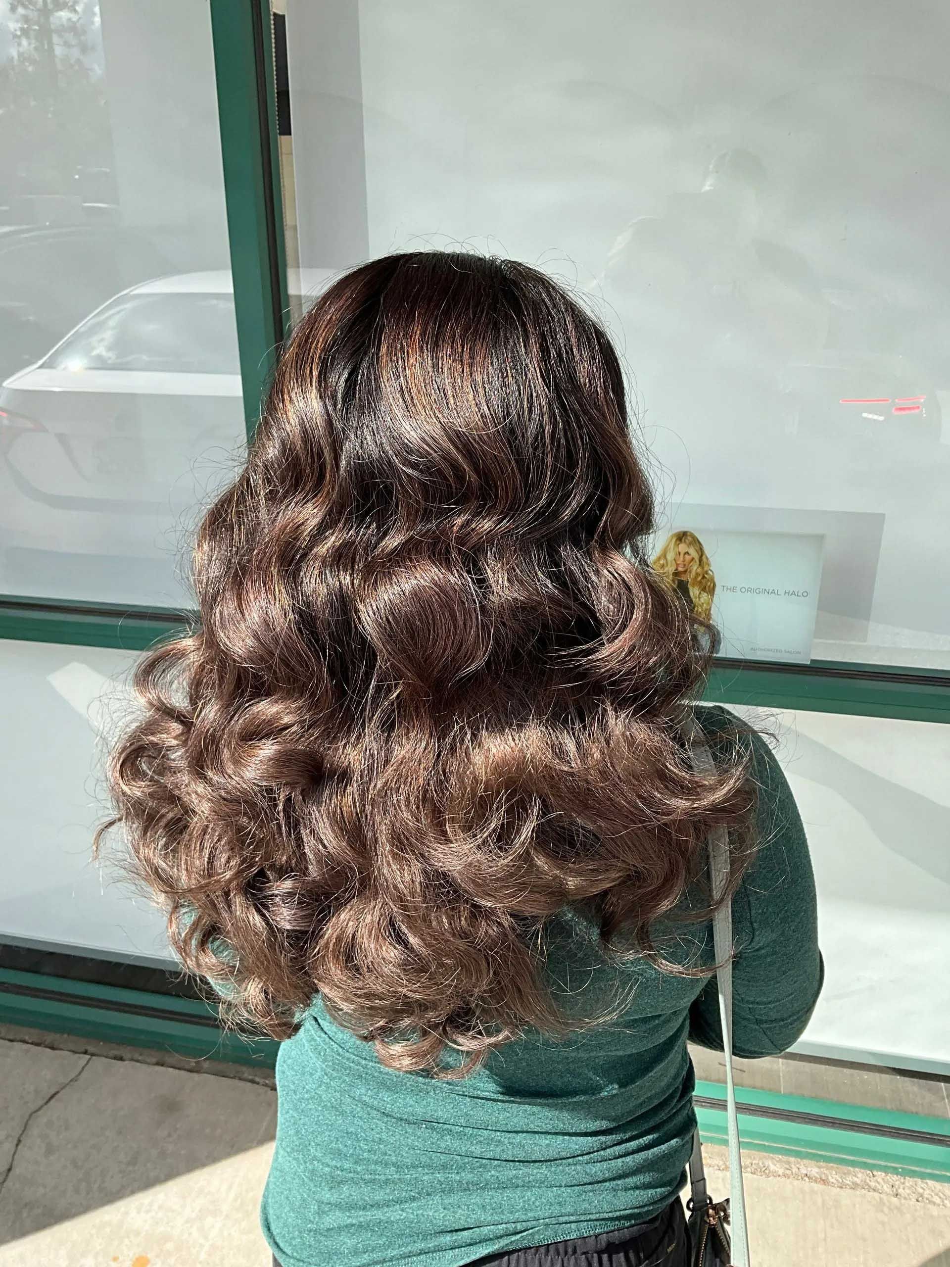 Person with wavy brown hair, standing outside, wearing a green shirt.