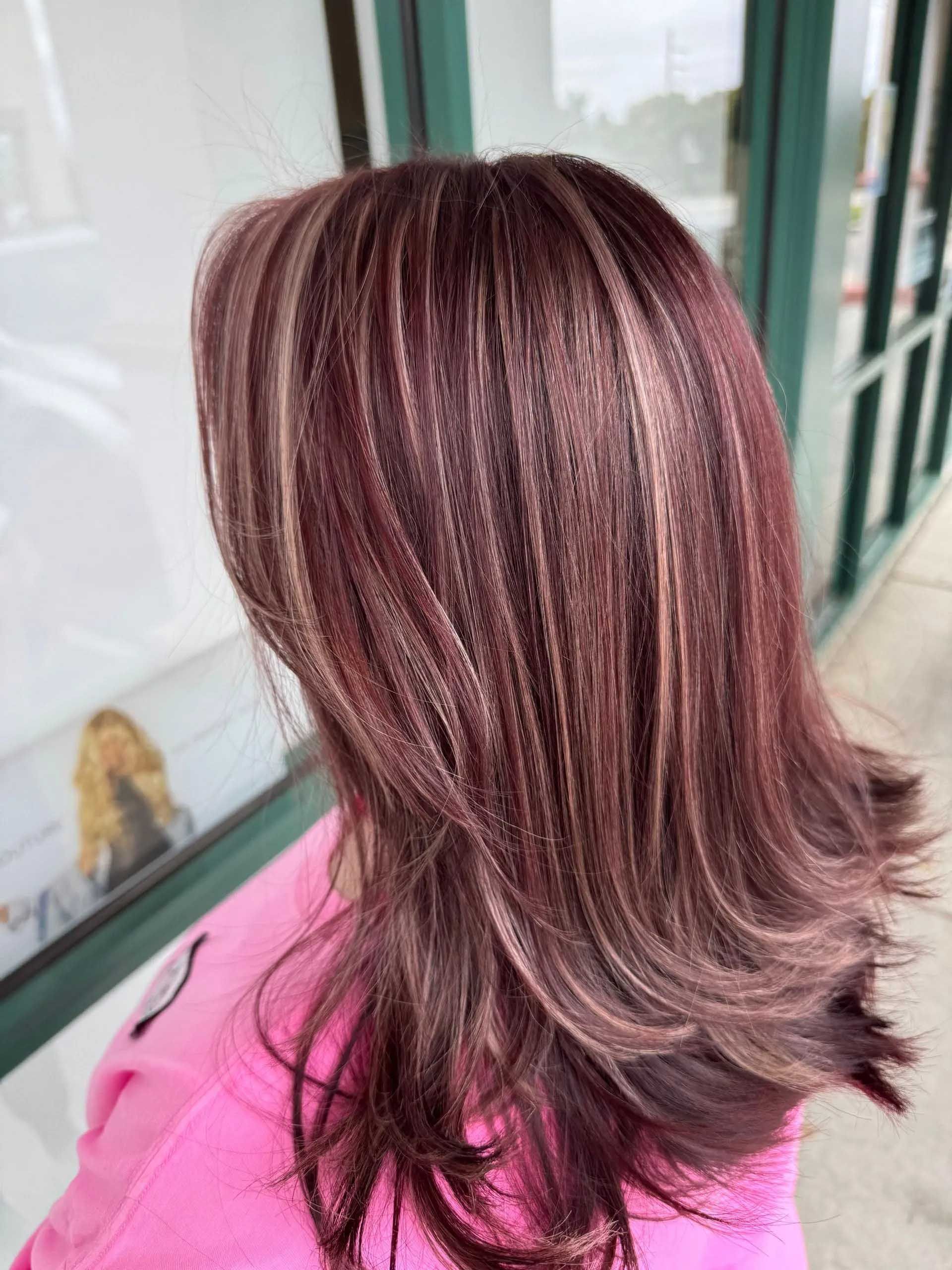 Woman with layered auburn hair with blonde and brown highlights, outdoors near a window.