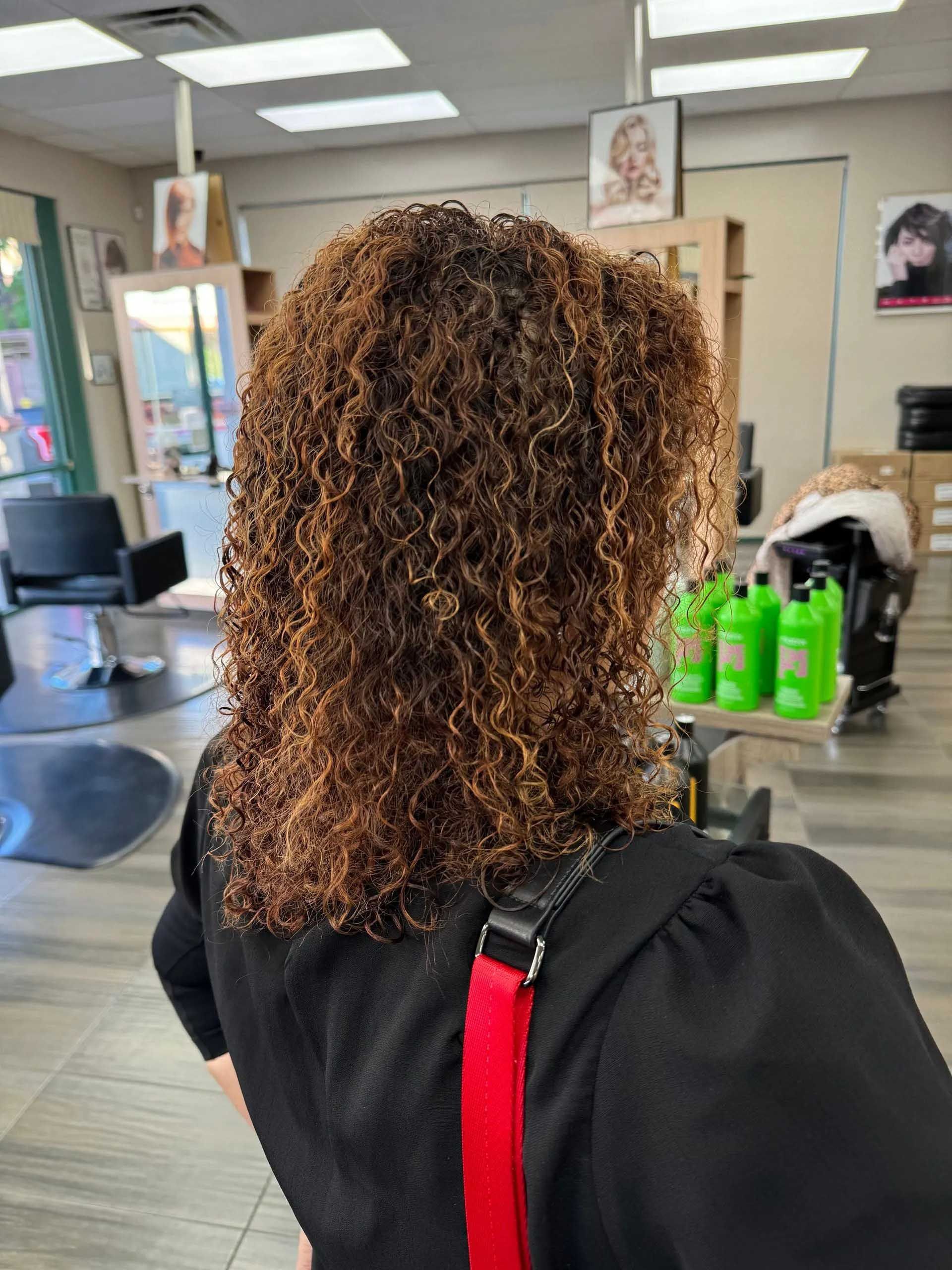 Woman with curly, brown hair in a salon, wearing a black top and red strap bag.