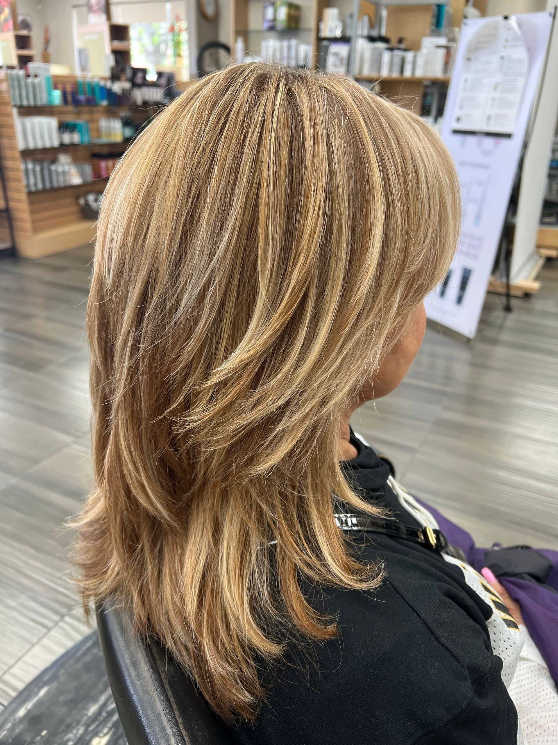 Woman with layered, crimped blonde and brown hair, sitting in a salon.