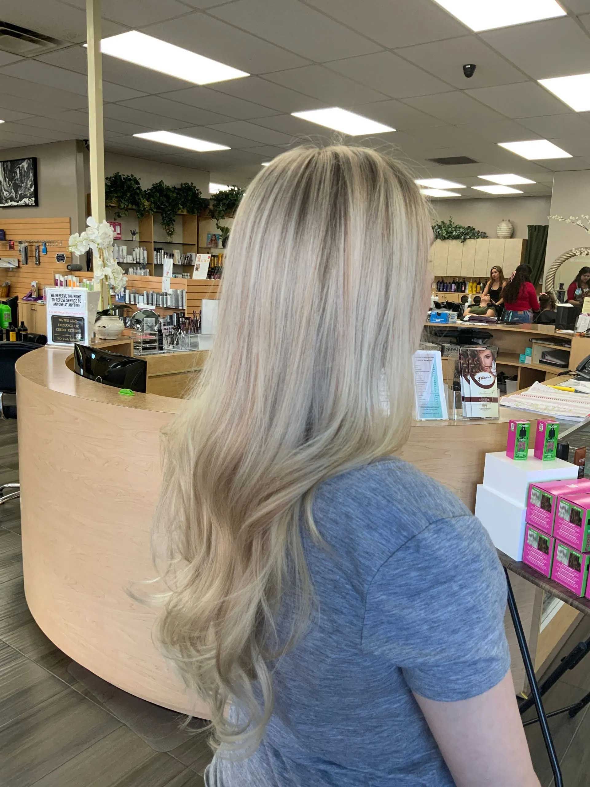 Woman with long, blonde hair styled in waves; inside a hair salon.