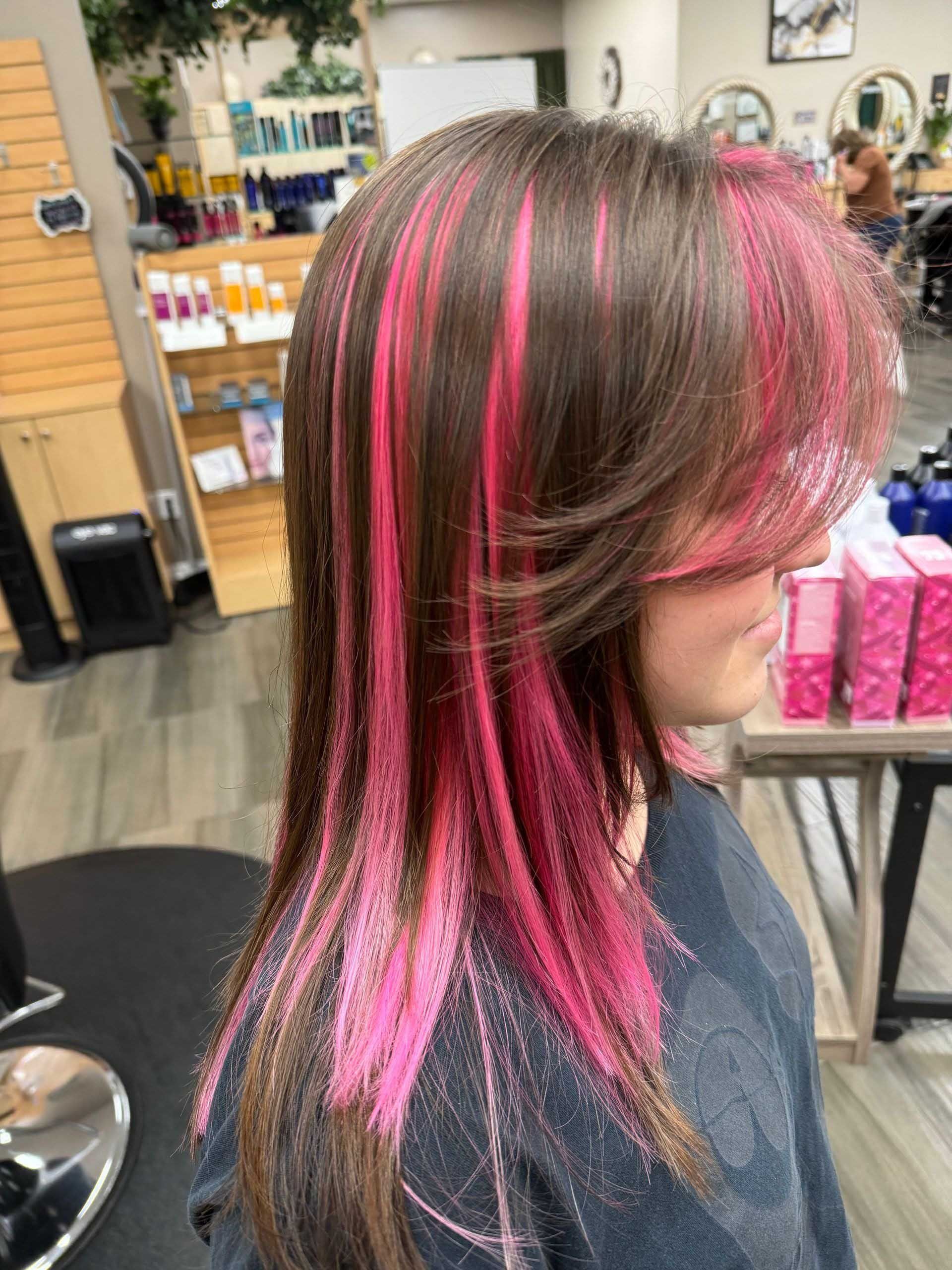 Woman with brown hair, layers, and bright pink streaks, in a salon setting.