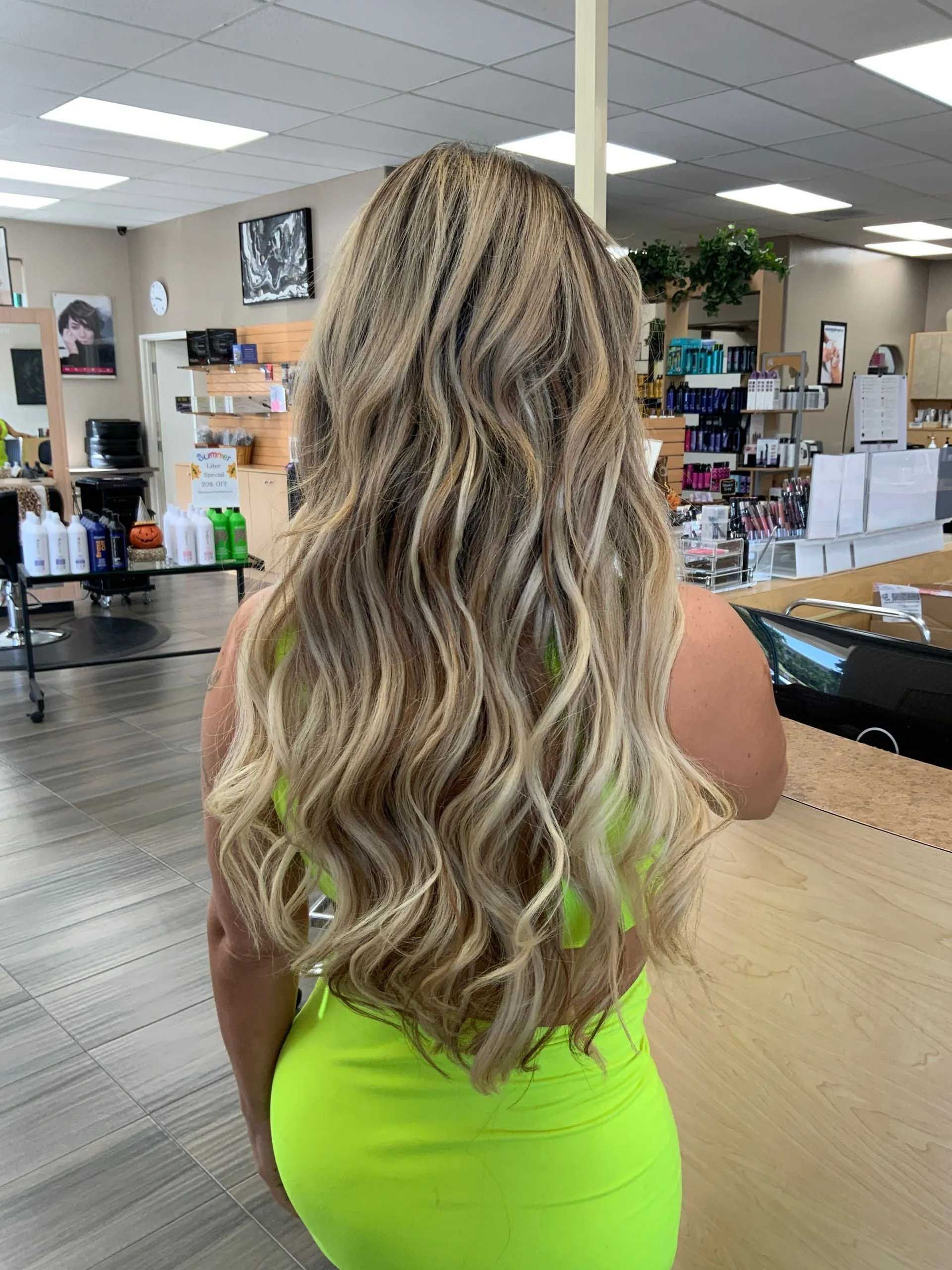 Woman with long, wavy blonde hair in a salon, wearing a neon green dress.