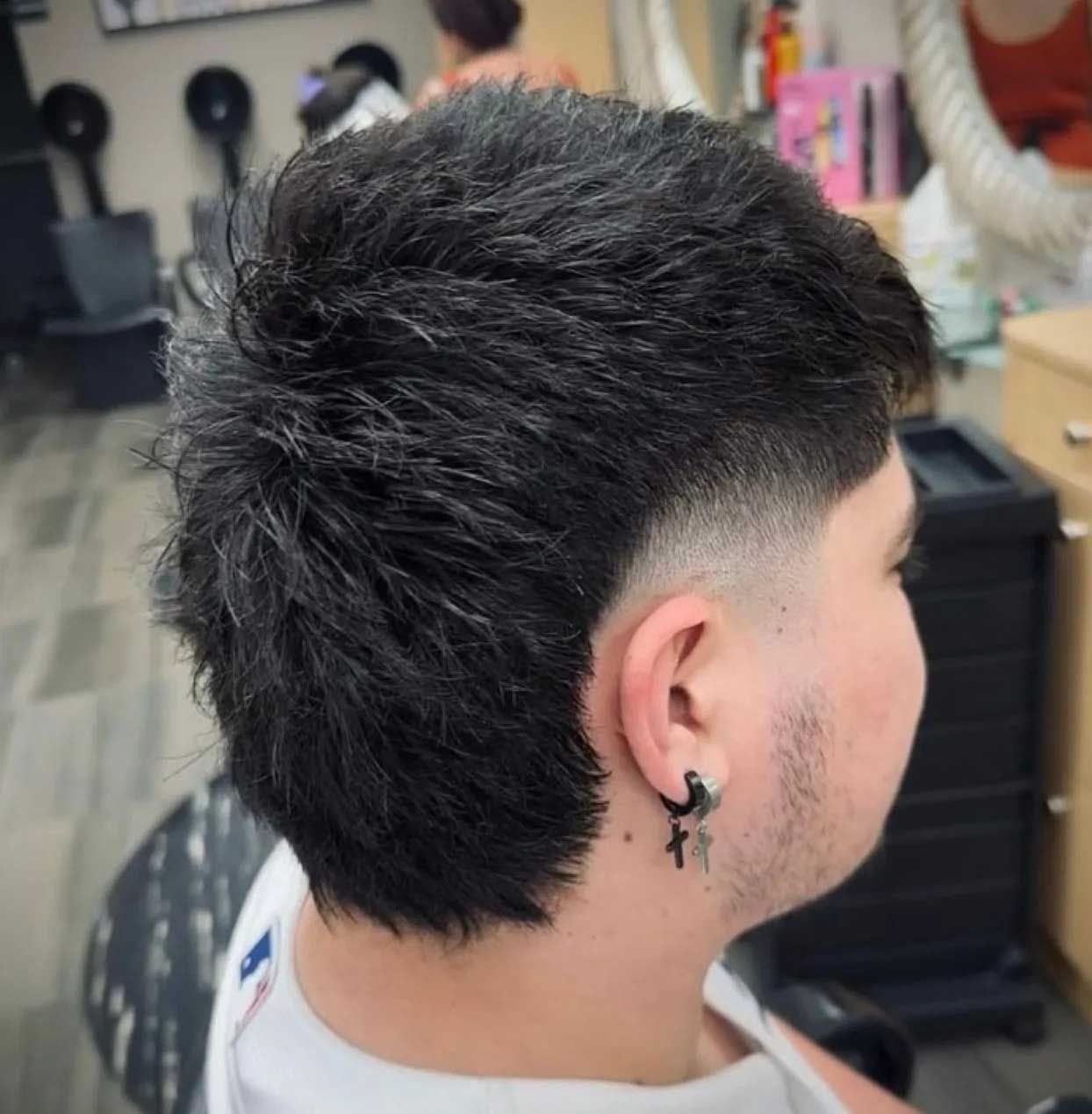 Man with dark hair, a mullet style haircut, in a salon. The sides are faded, and he's wearing an earring.