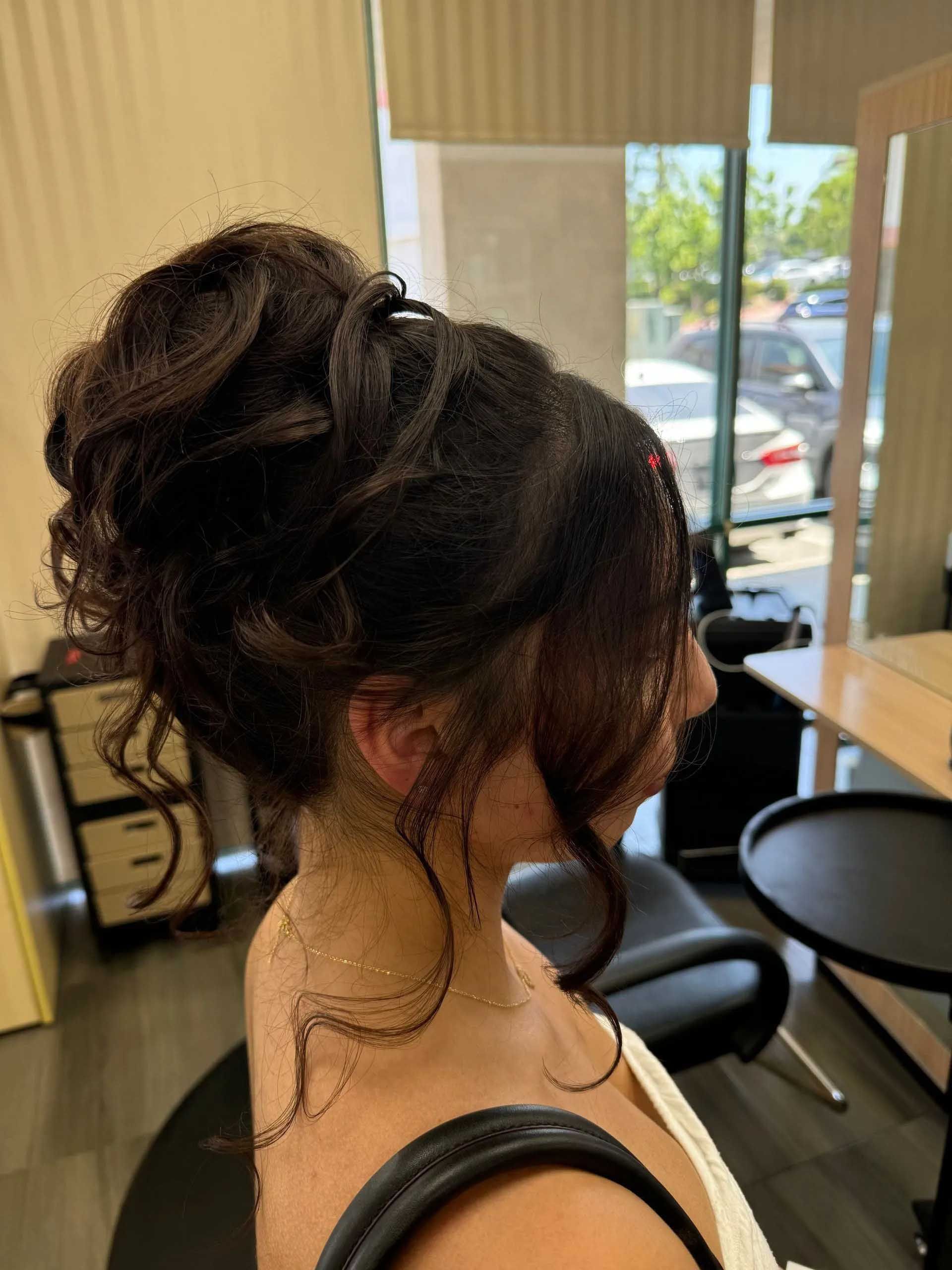 Woman with dark hair in an updo, with loose curls framing her face, indoors at a salon.
