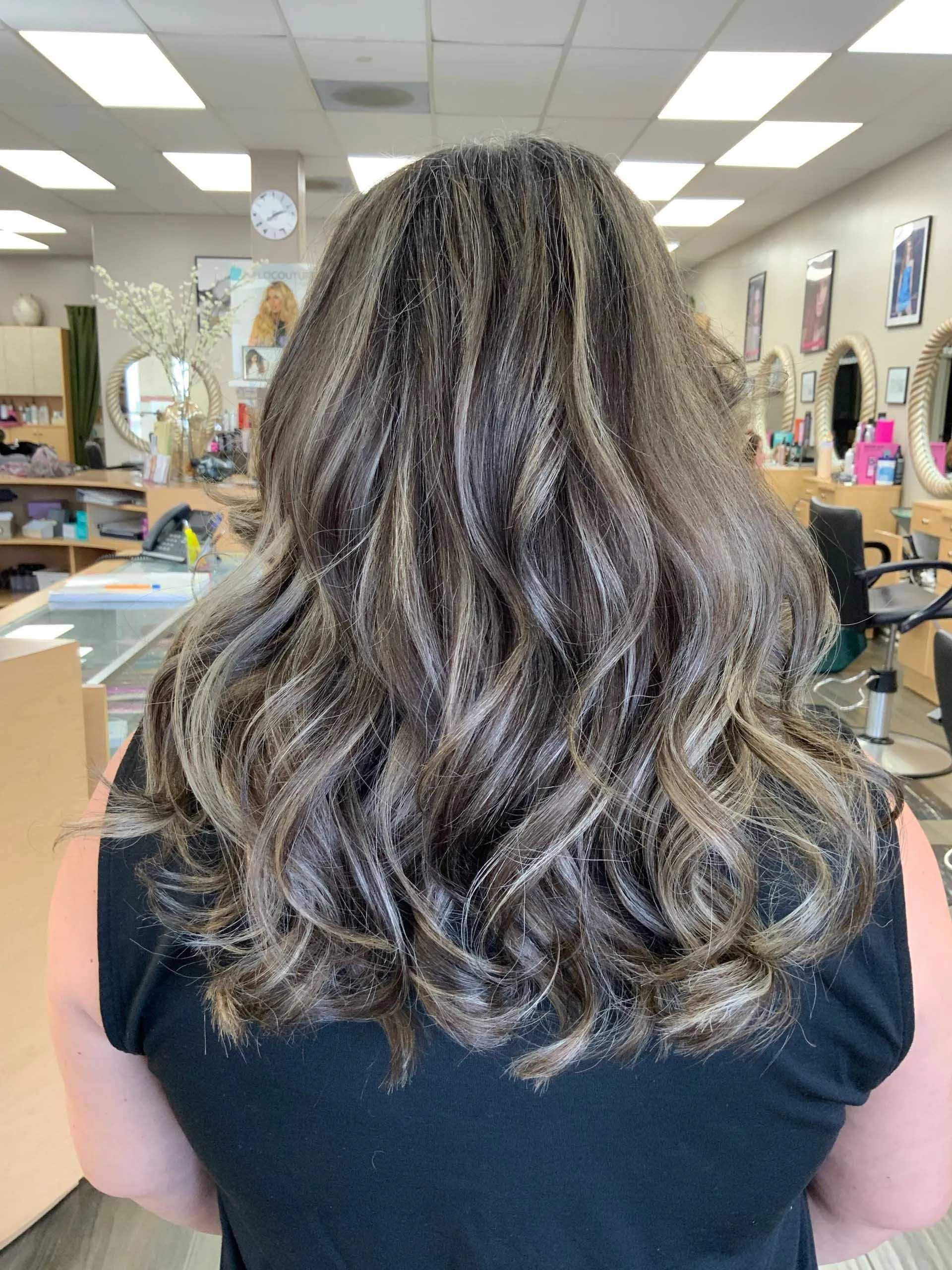 Woman's wavy, highlighted hair; salon setting. Brown hair with lighter streaks. Back view.