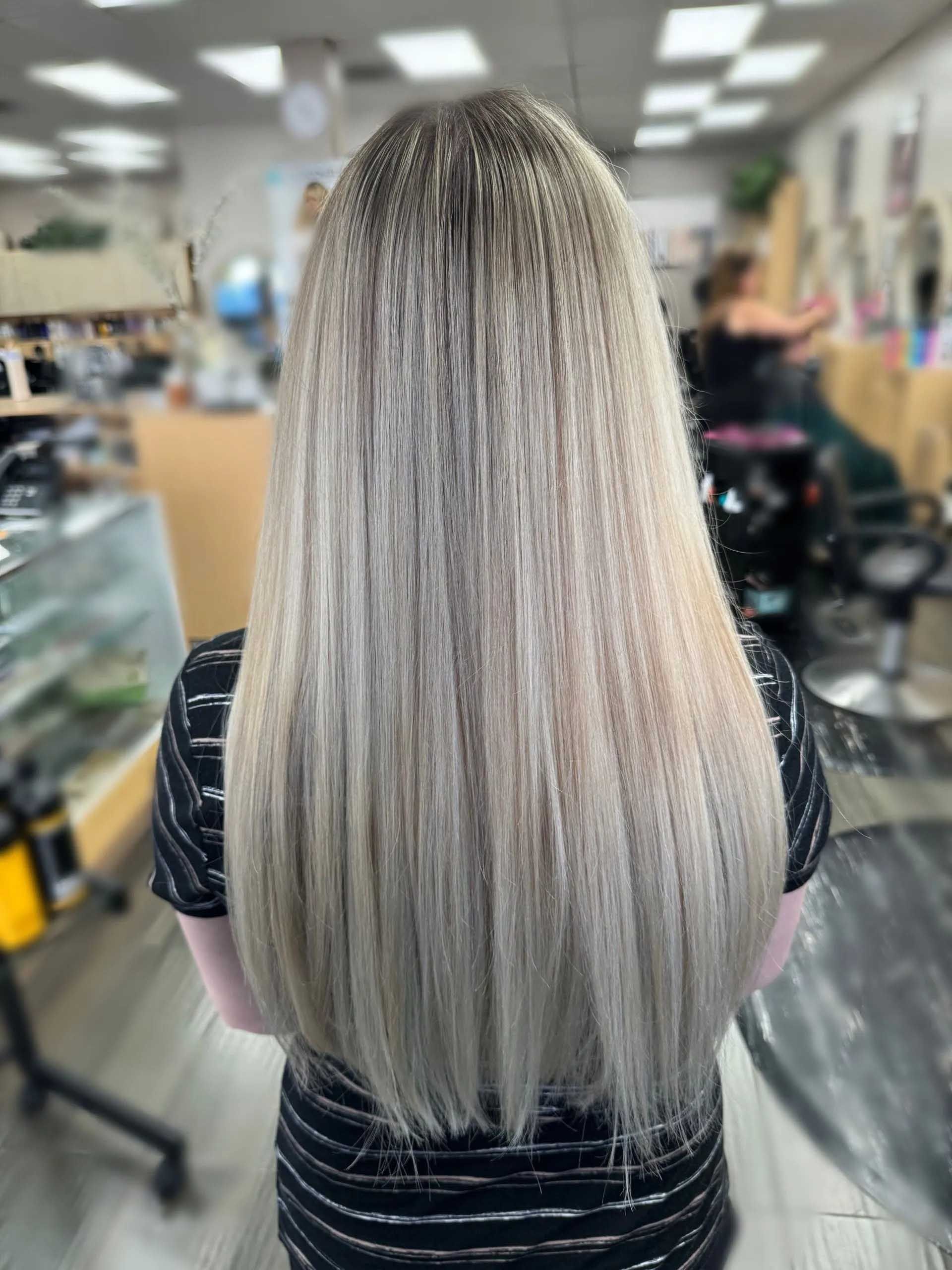 Long, straight blonde hair with dark roots, in a salon setting.