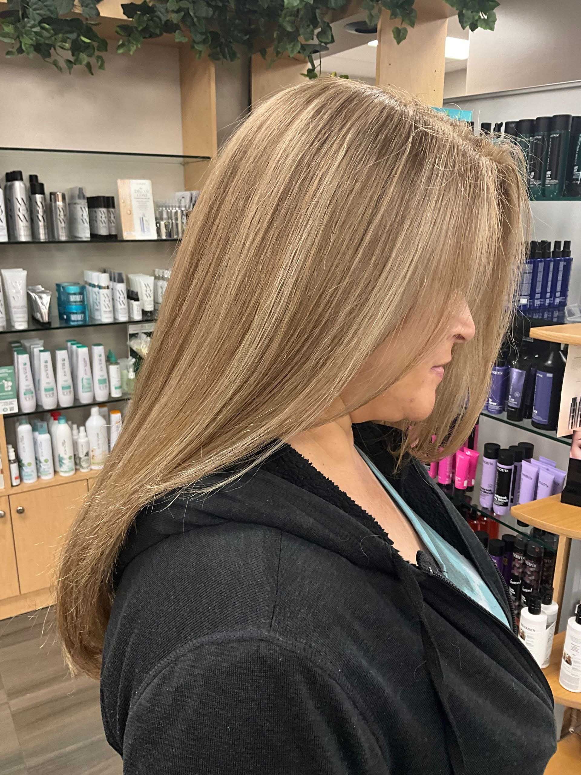 Woman with long, light-brown textured hair, wearing a black robe, in a salon setting. Hair obscures her face.