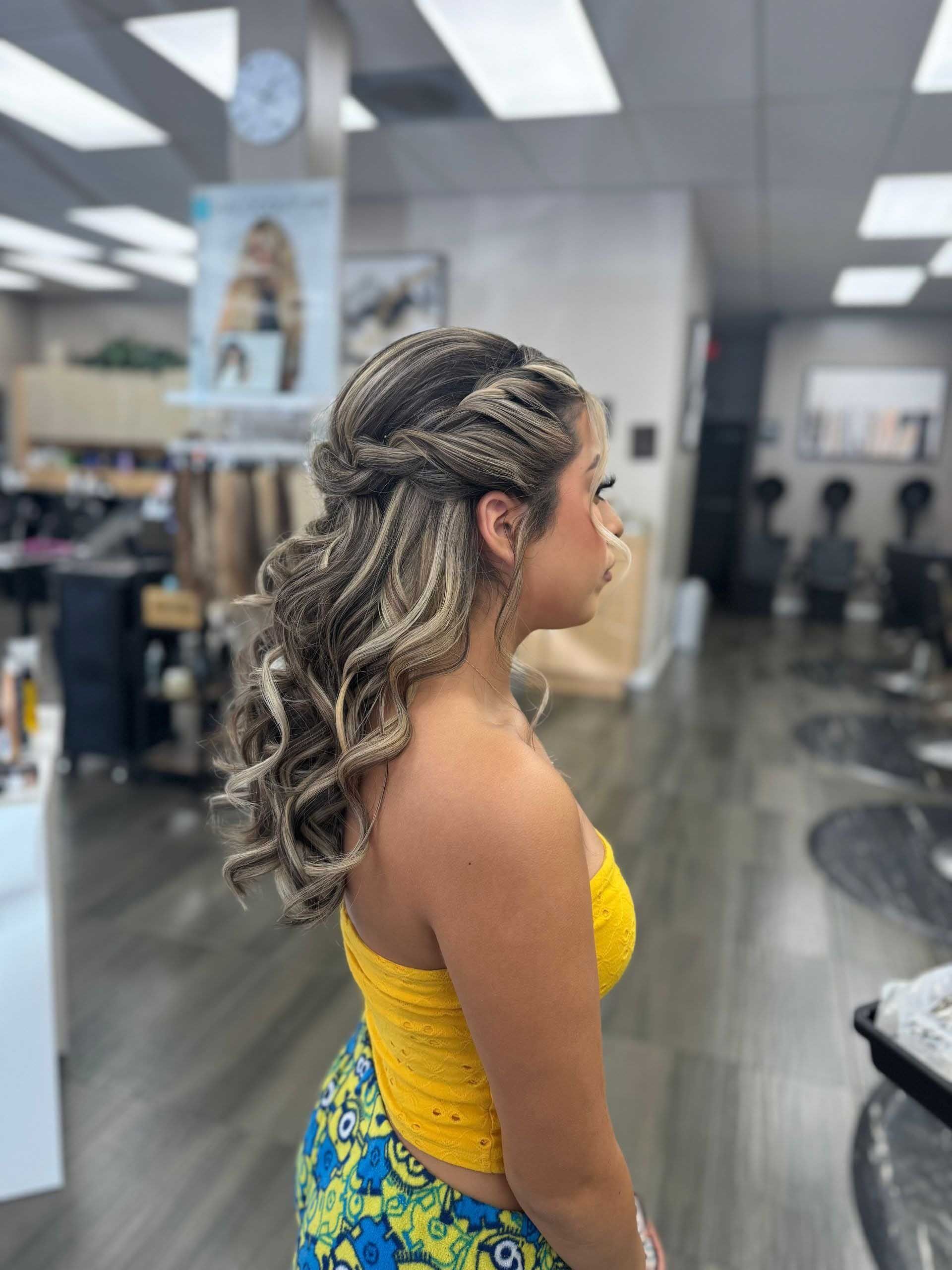 Woman with braided hairstyle, wearing yellow top and patterned pants, in a hair salon.