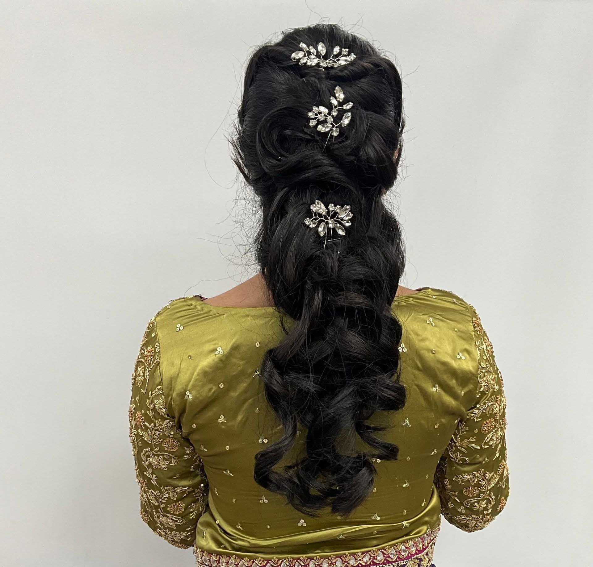 Woman with dark hair in a formal updo with jeweled hair accessories, wearing a gold embellished top.