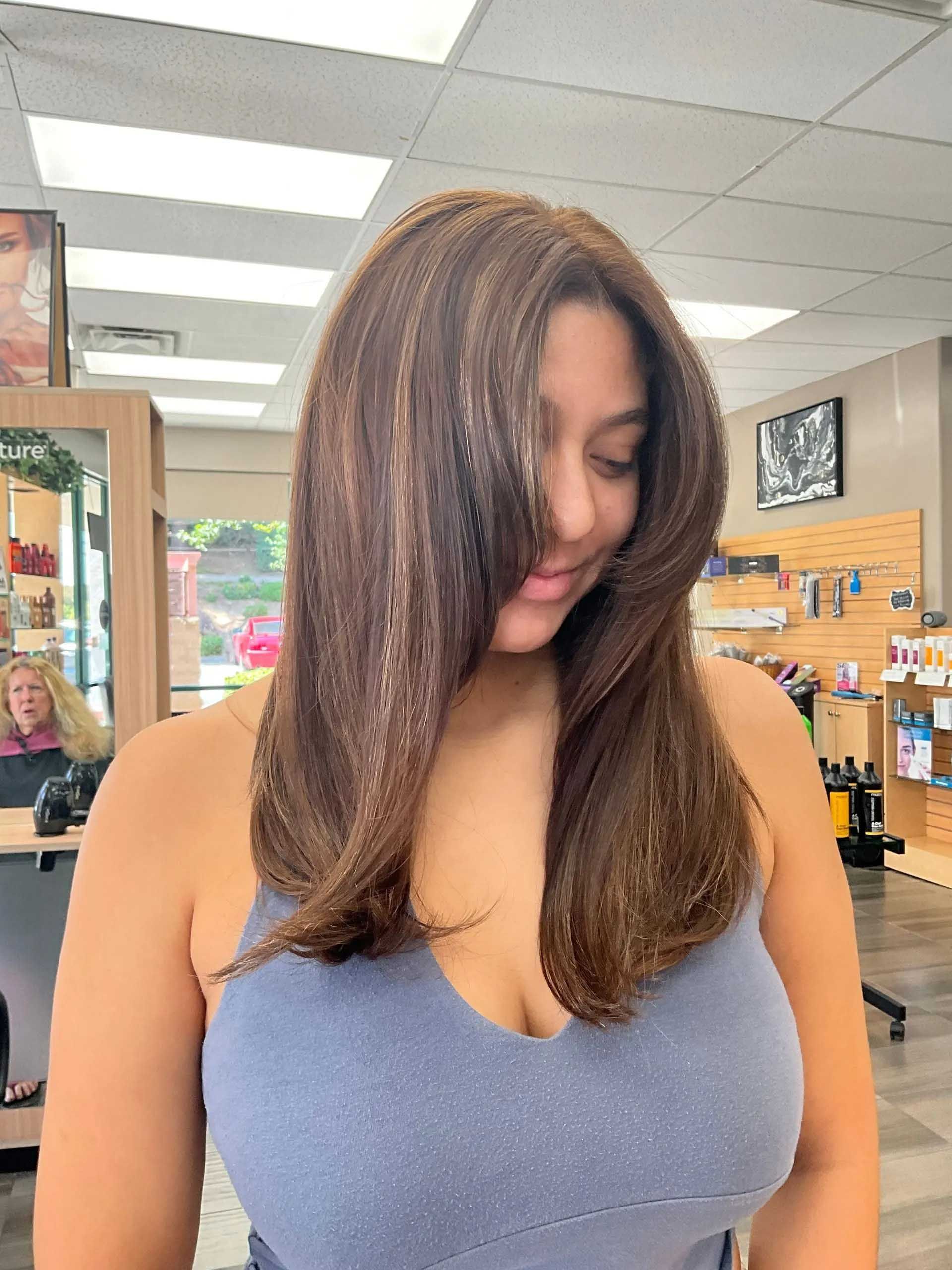 Woman with layered brown hair, highlights, and blue tank top; salon setting.