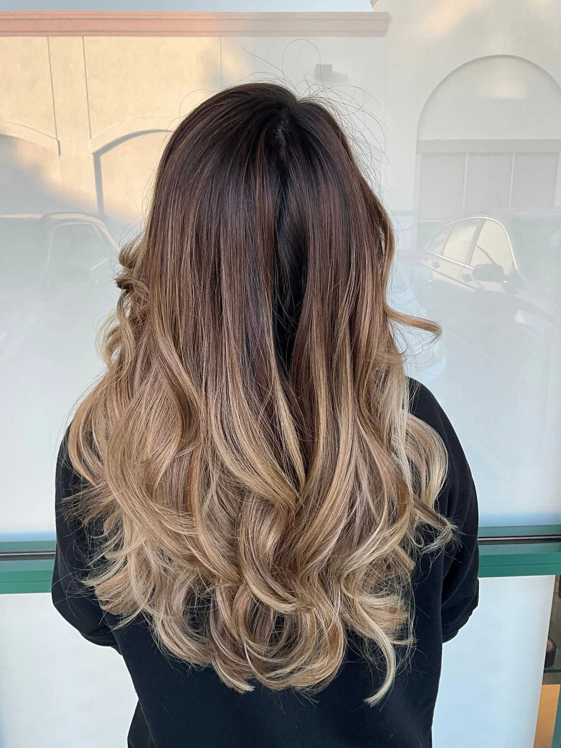 Woman with dark to light brown ombre hair, styled with curls.