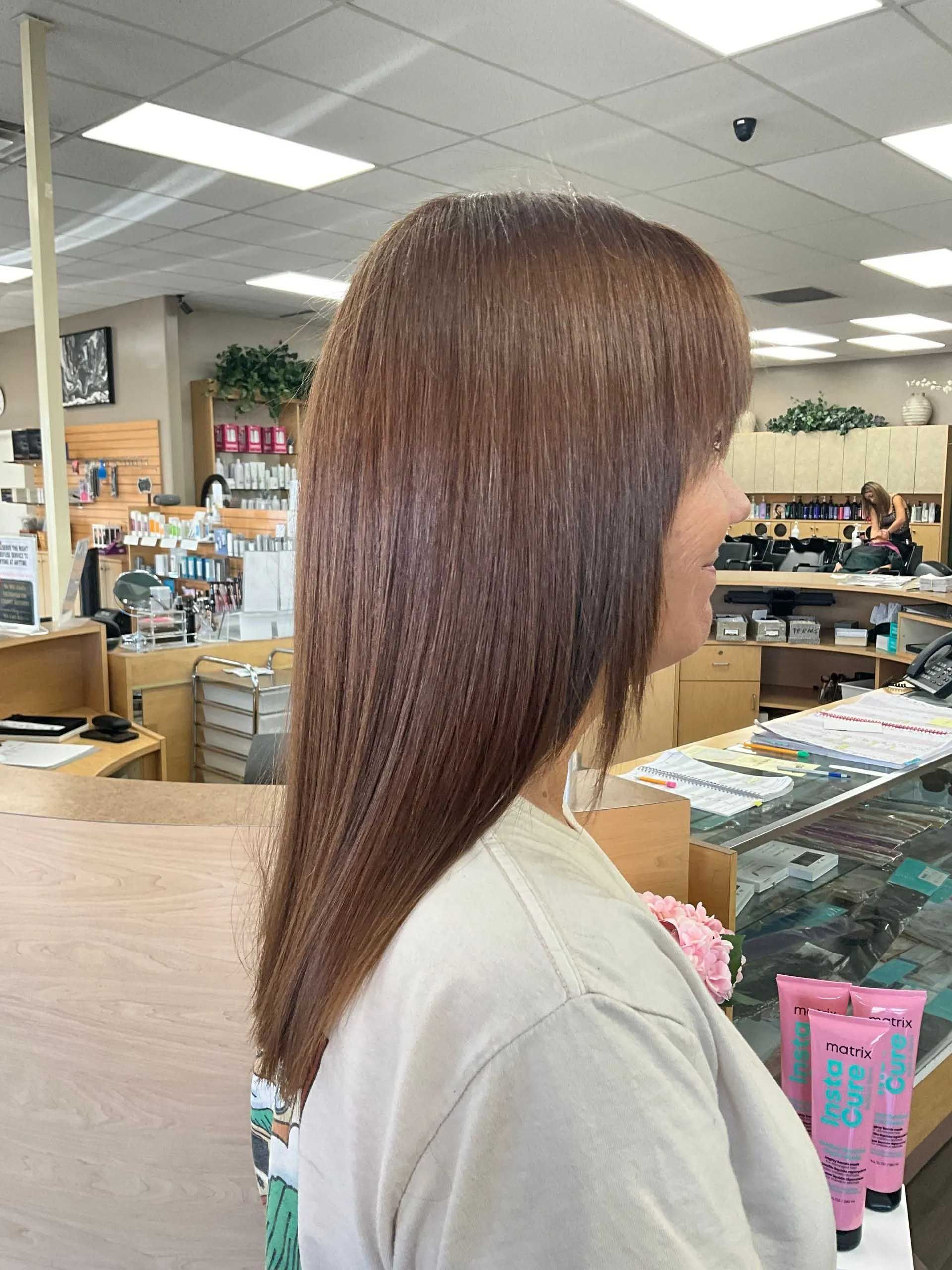 Woman with long, straight brown hair in a salon setting, wearing a light-colored shirt.