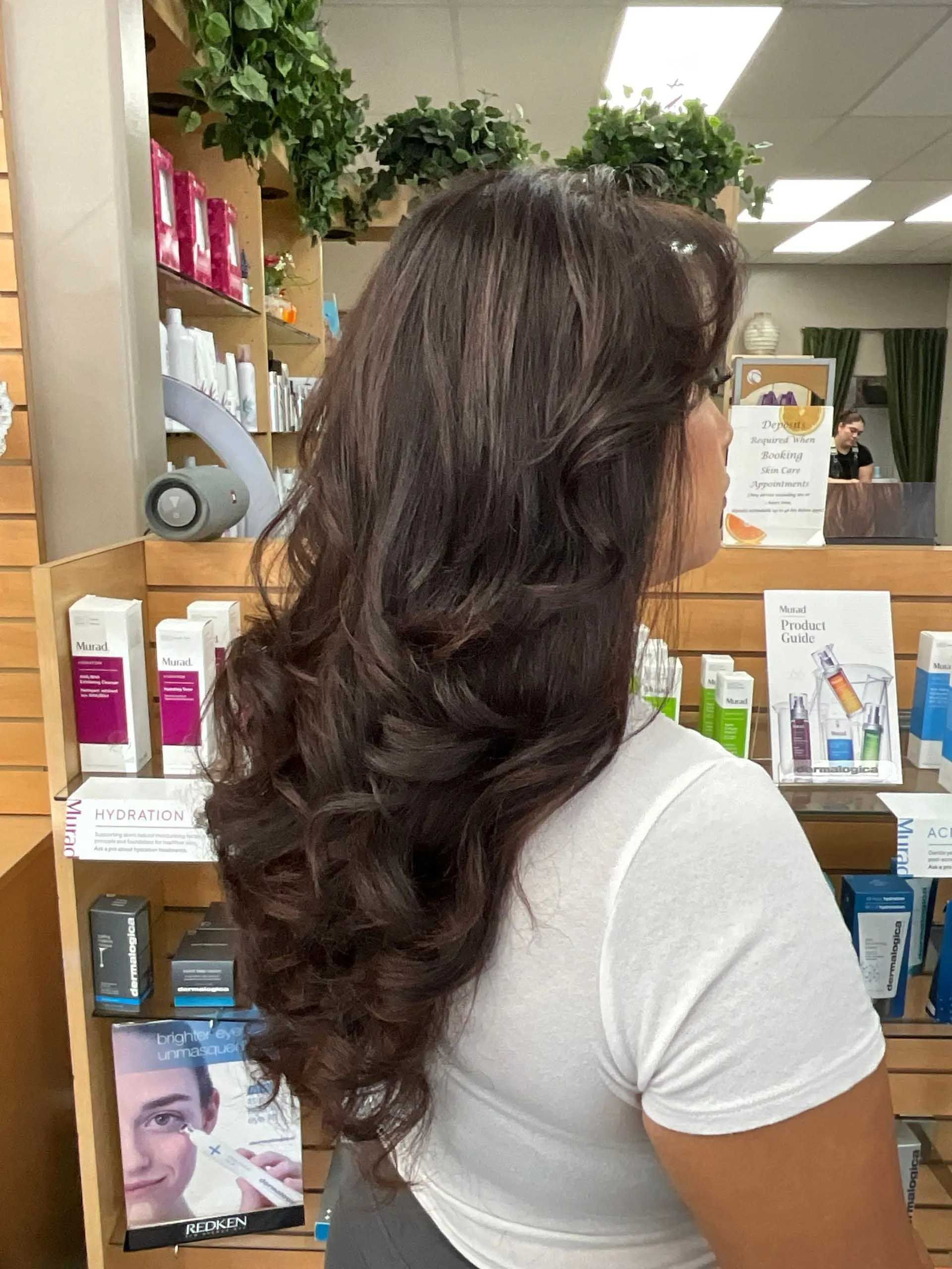 Woman with long, layered brown hair in a retail setting, looking right.