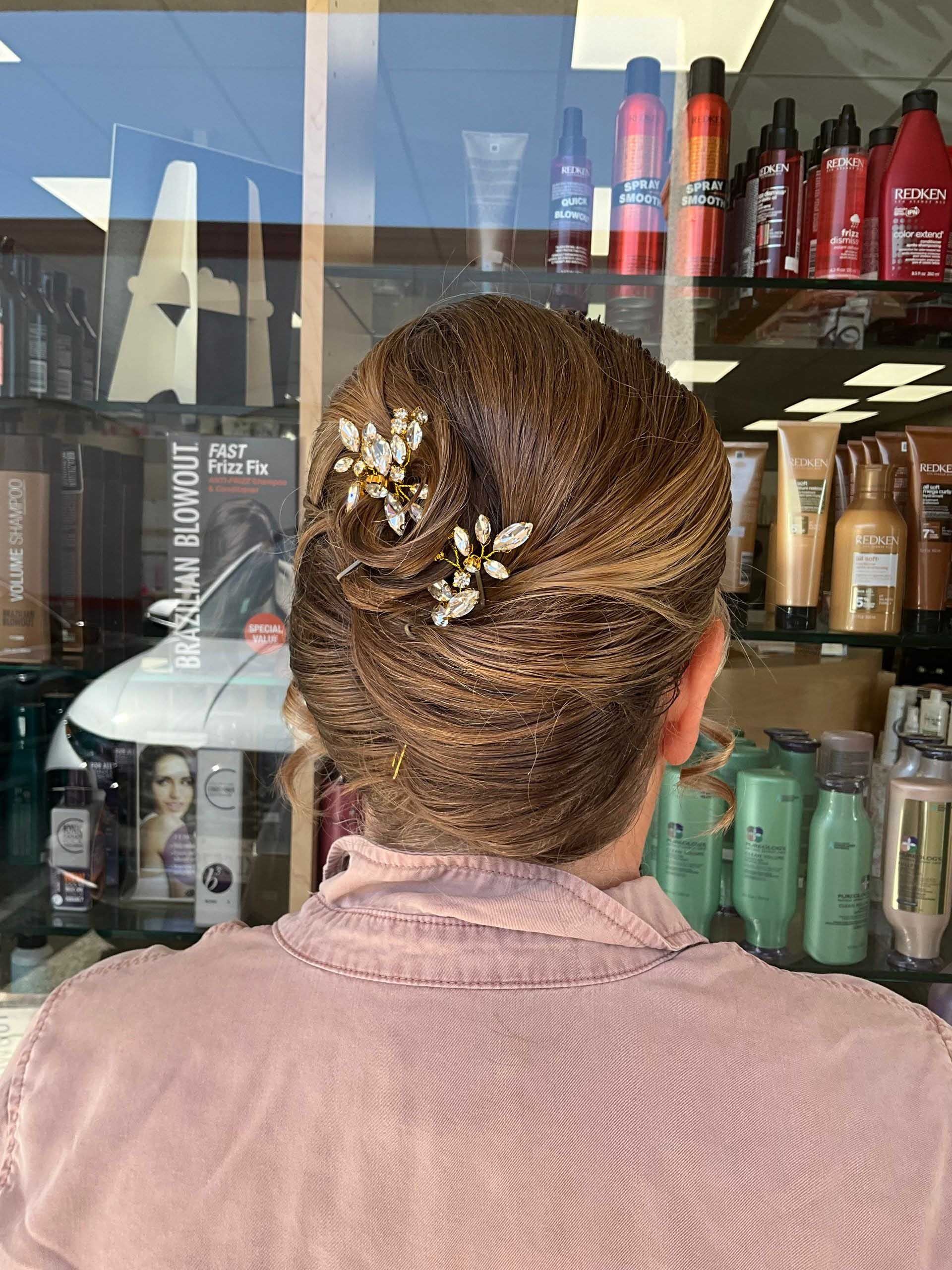 Woman with updo hairstyle, two jeweled hair accessories, in front of hair products in a salon.