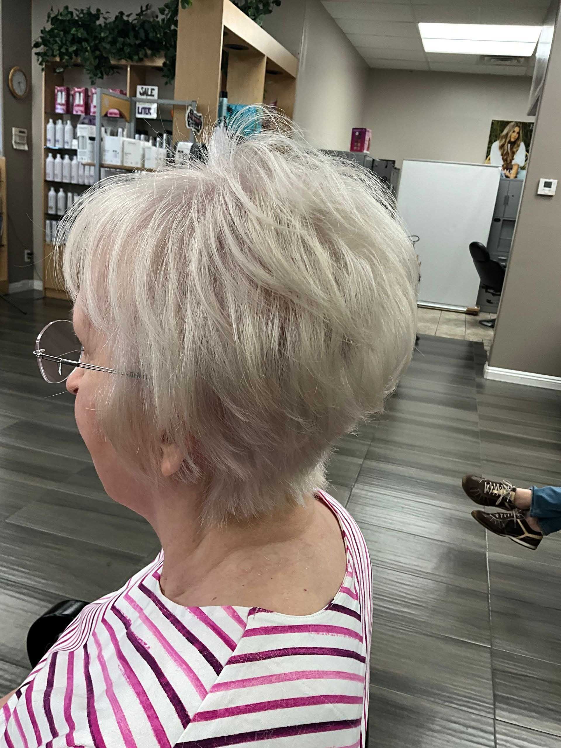 Woman with short, light-colored hair in a salon chair, wearing a striped shirt.