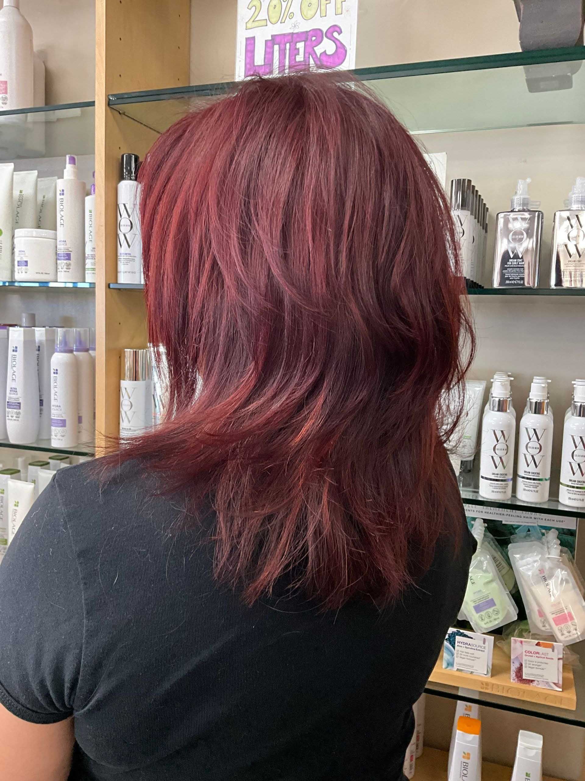 Woman with red hair standing in a hair product store, back to camera.