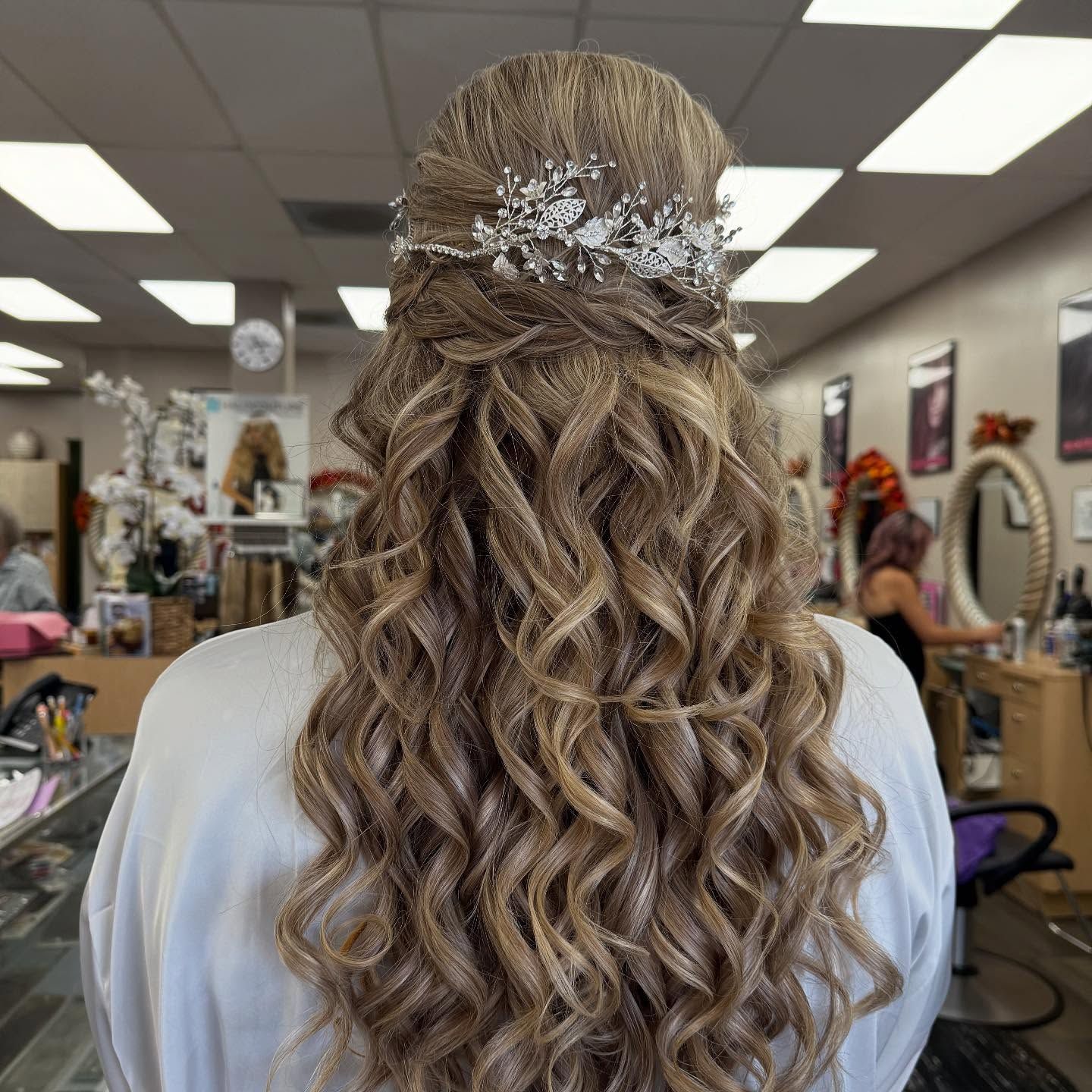 Woman with curly, light brown hair styled up with a decorative headpiece in a salon setting.