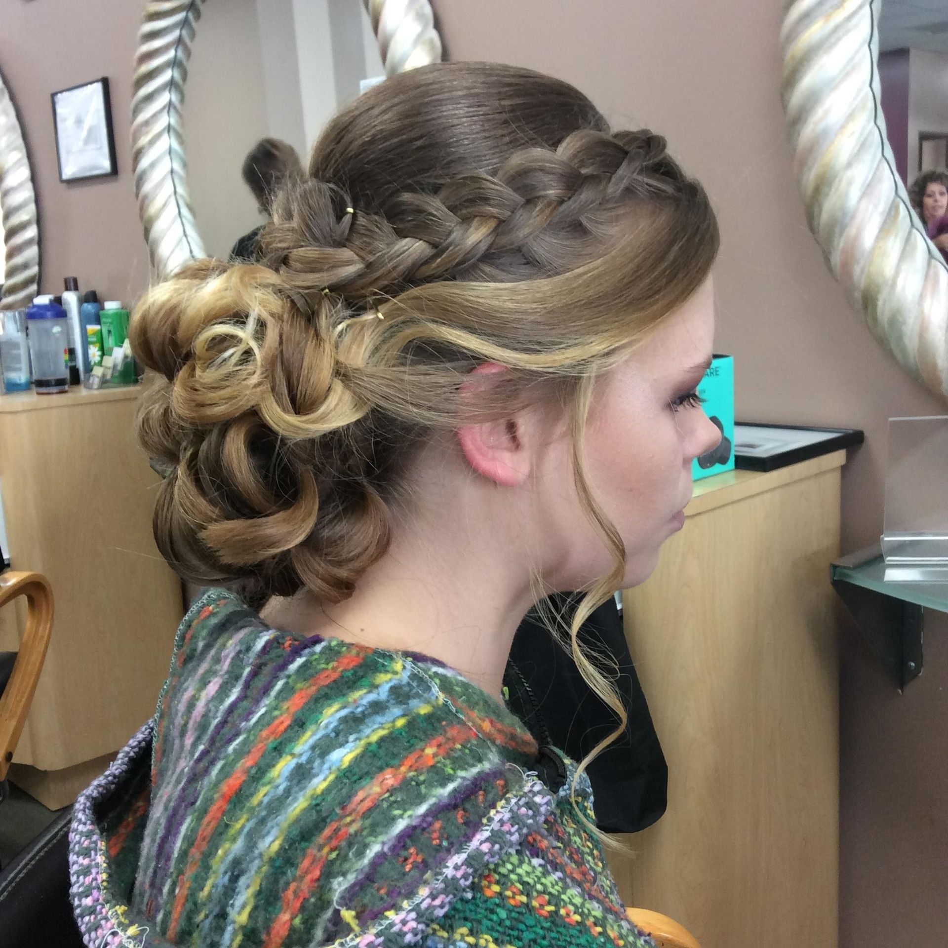 Woman with blonde hair in an updo style with a braided crown, inside a salon.