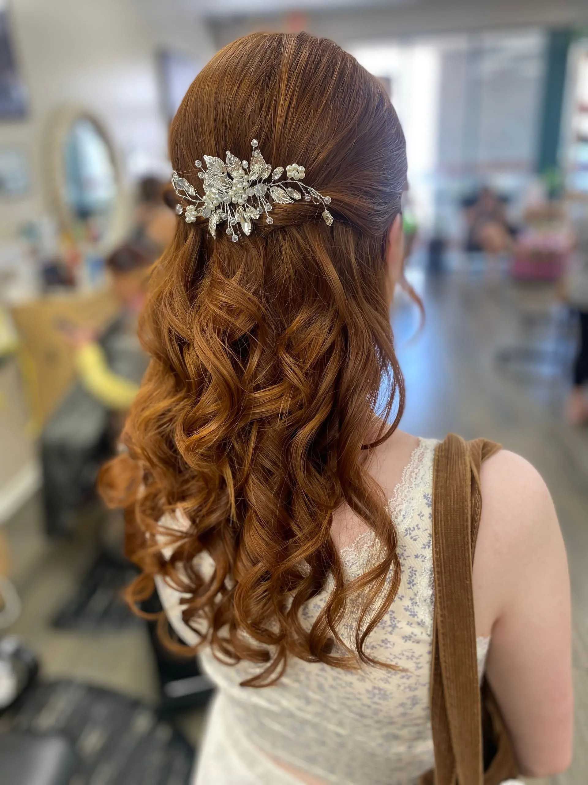 Woman with red curly hair in a half-up style, wearing a jeweled hairpiece, in a salon.