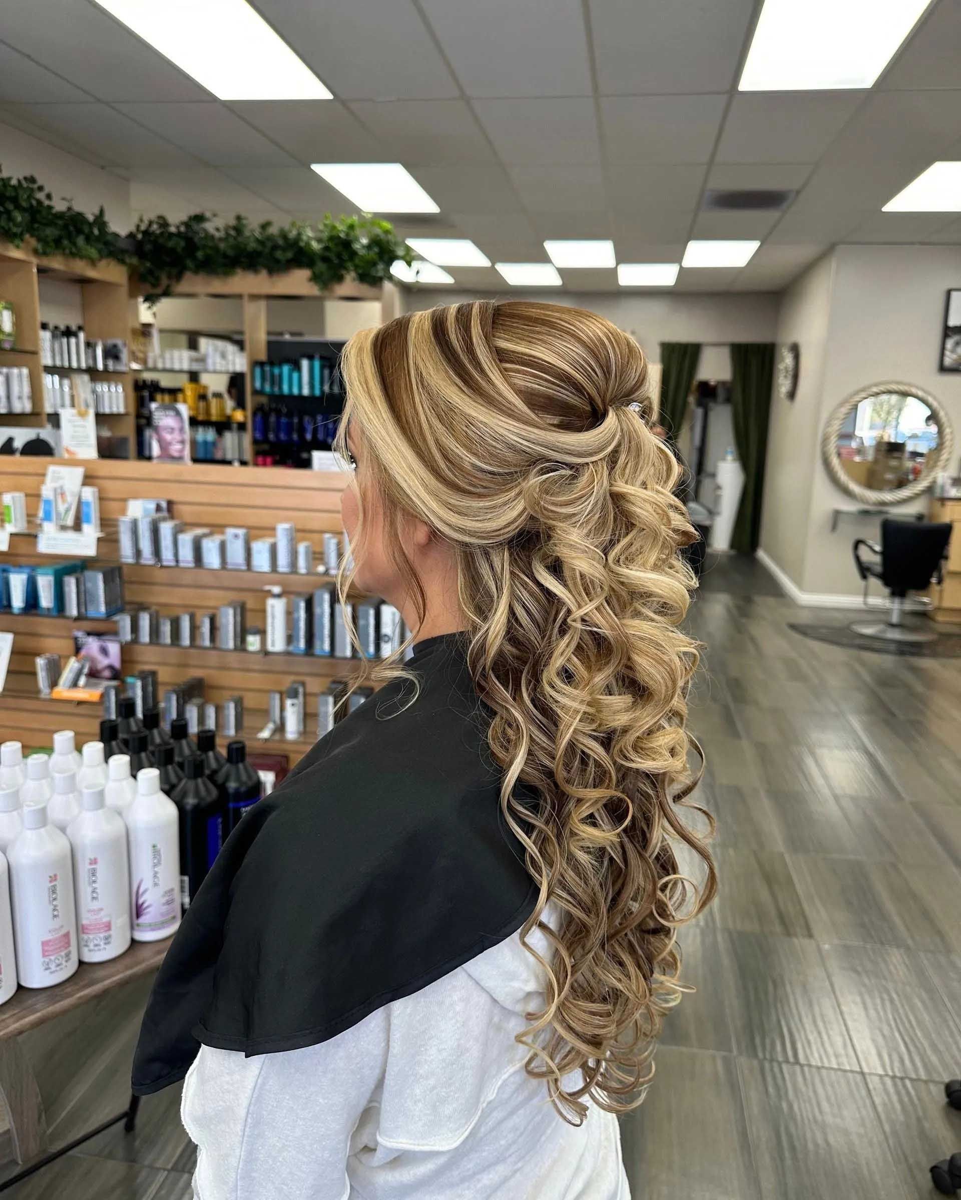 Woman with curly, light brown hair styled in an updo and cascading curls in a salon.