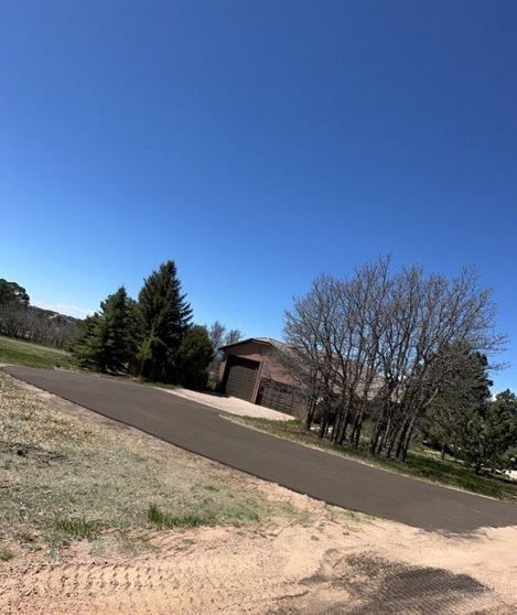 Paved road leading uphill to a building with a garage. Trees and clear blue sky.