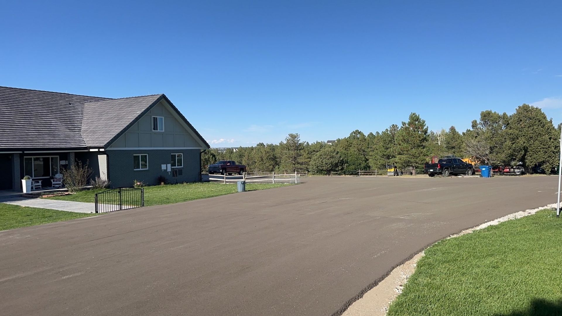 Gravel parking lot near a green building, several vehicles, and treeline under a blue sky.
