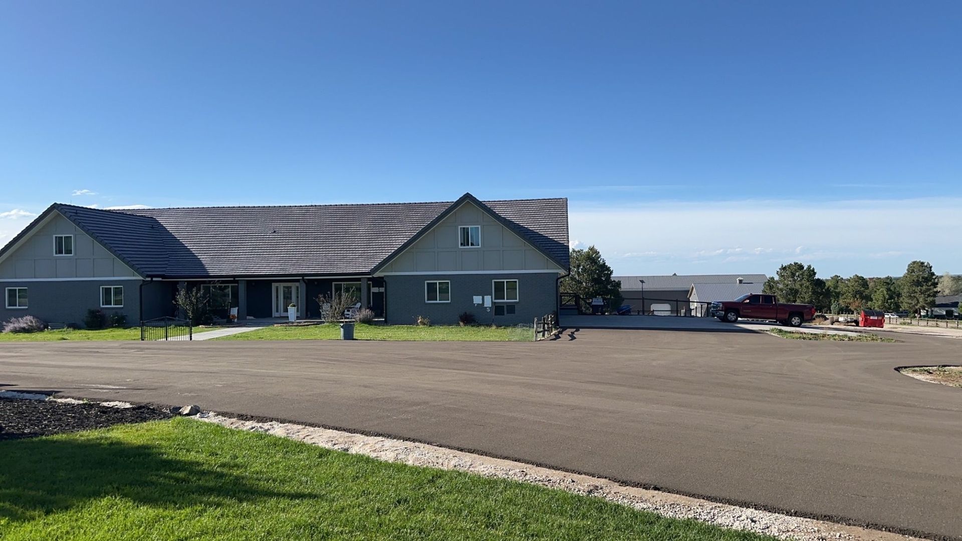 Grey building with a weathered roof and parking area under a blue sky.