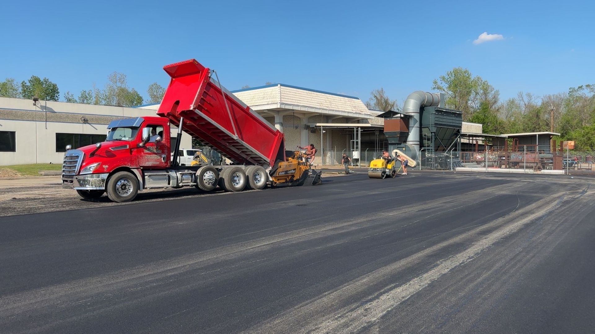 Red dump truck unloading asphalt for road paving.