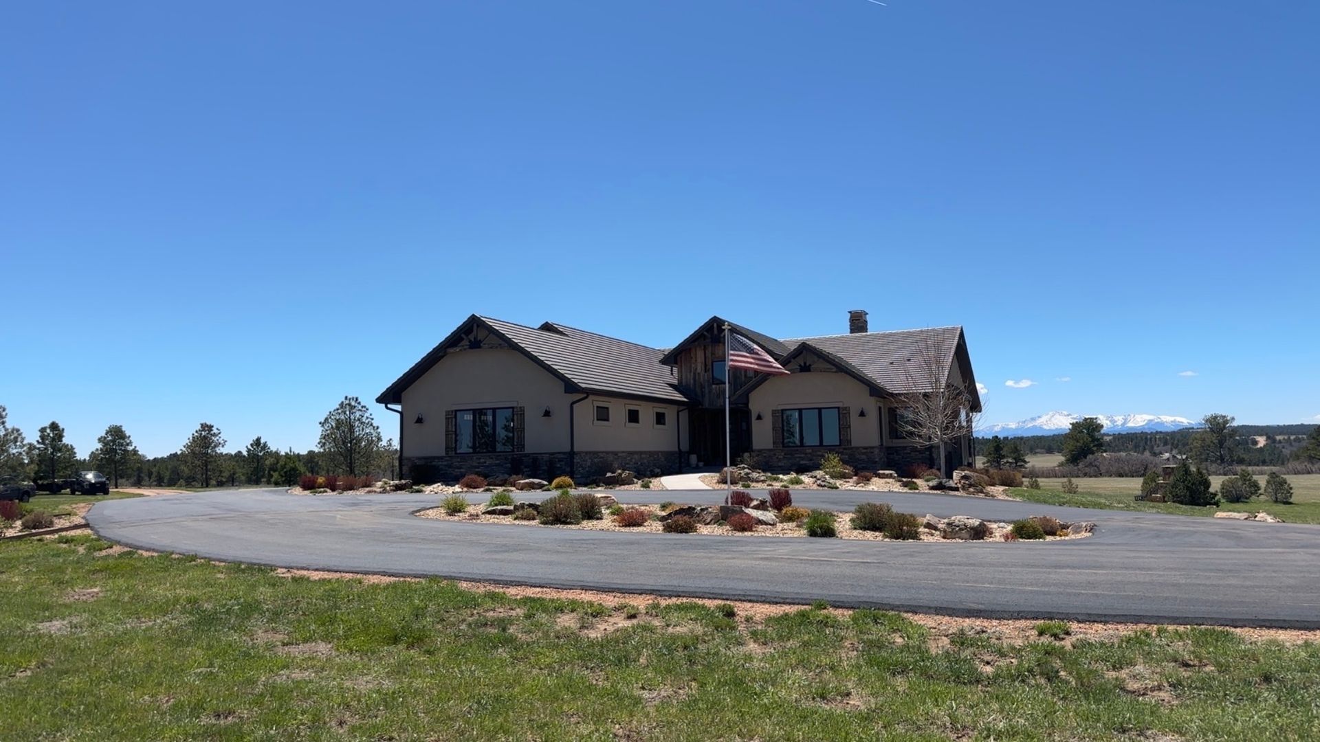 A large beige house with a stone facade and a circular driveway under a clear blue sky.