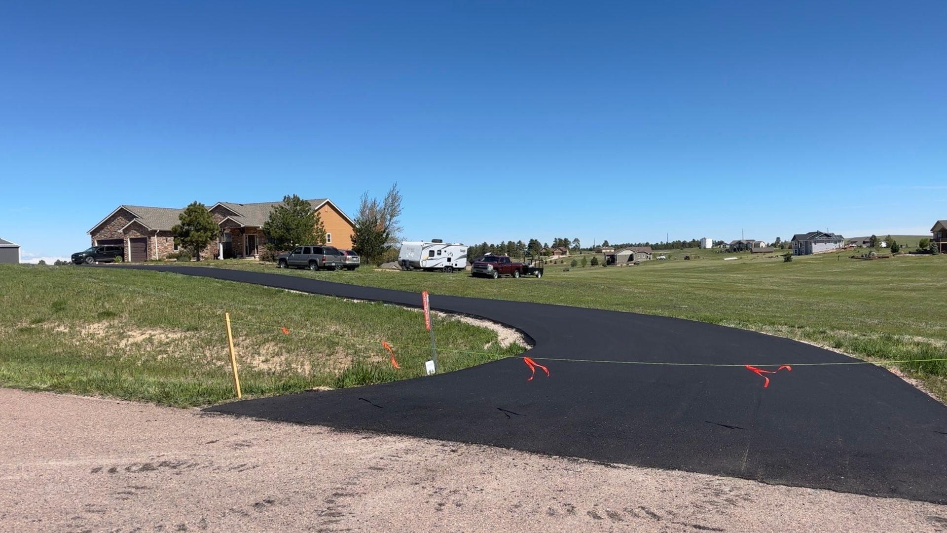 Newly paved driveway leads to a house on a sunny day. Orange cones mark the edges.