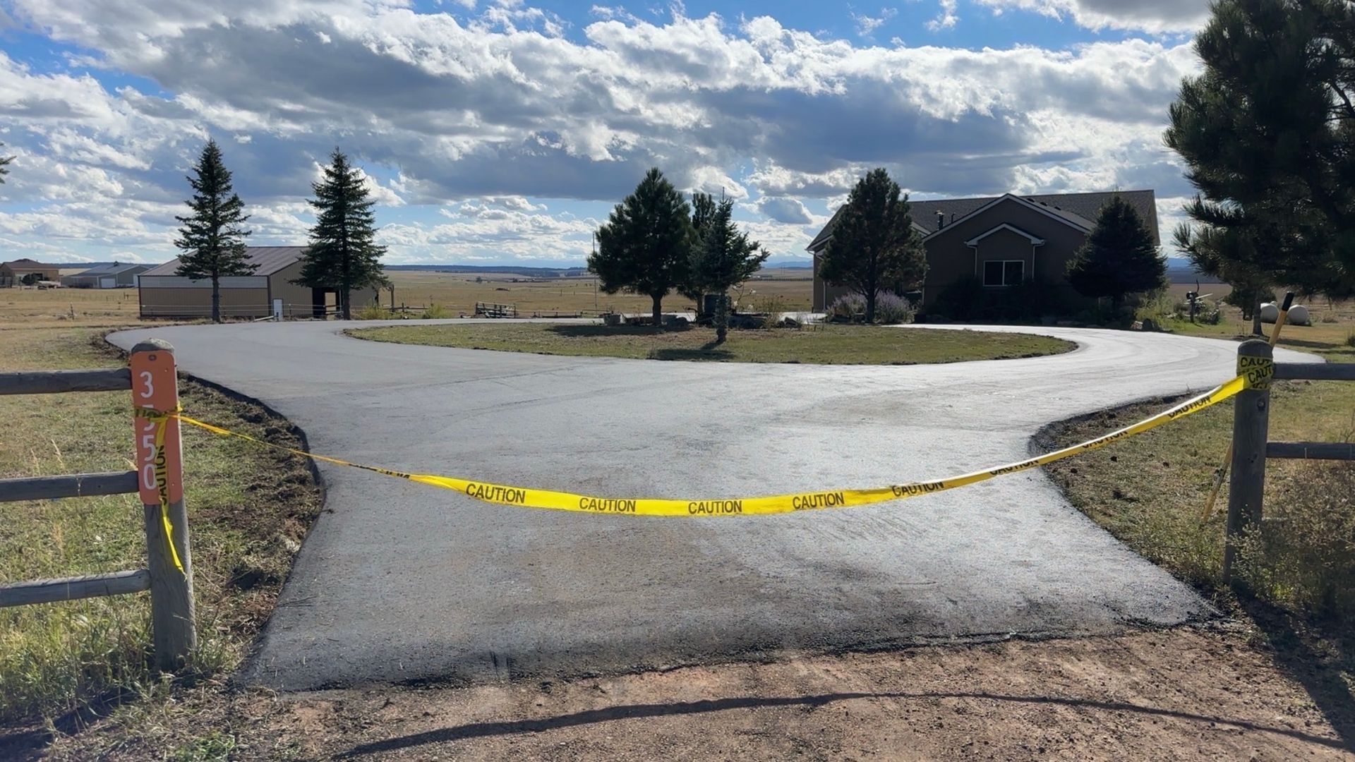 Newly paved circular driveway cordoned off with caution tape; house and trees in background.