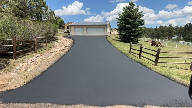 Newly paved asphalt driveway leading to a house with a garage, under a partly cloudy sky.