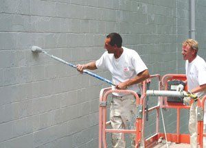 Two men painting a wall using a roller brush