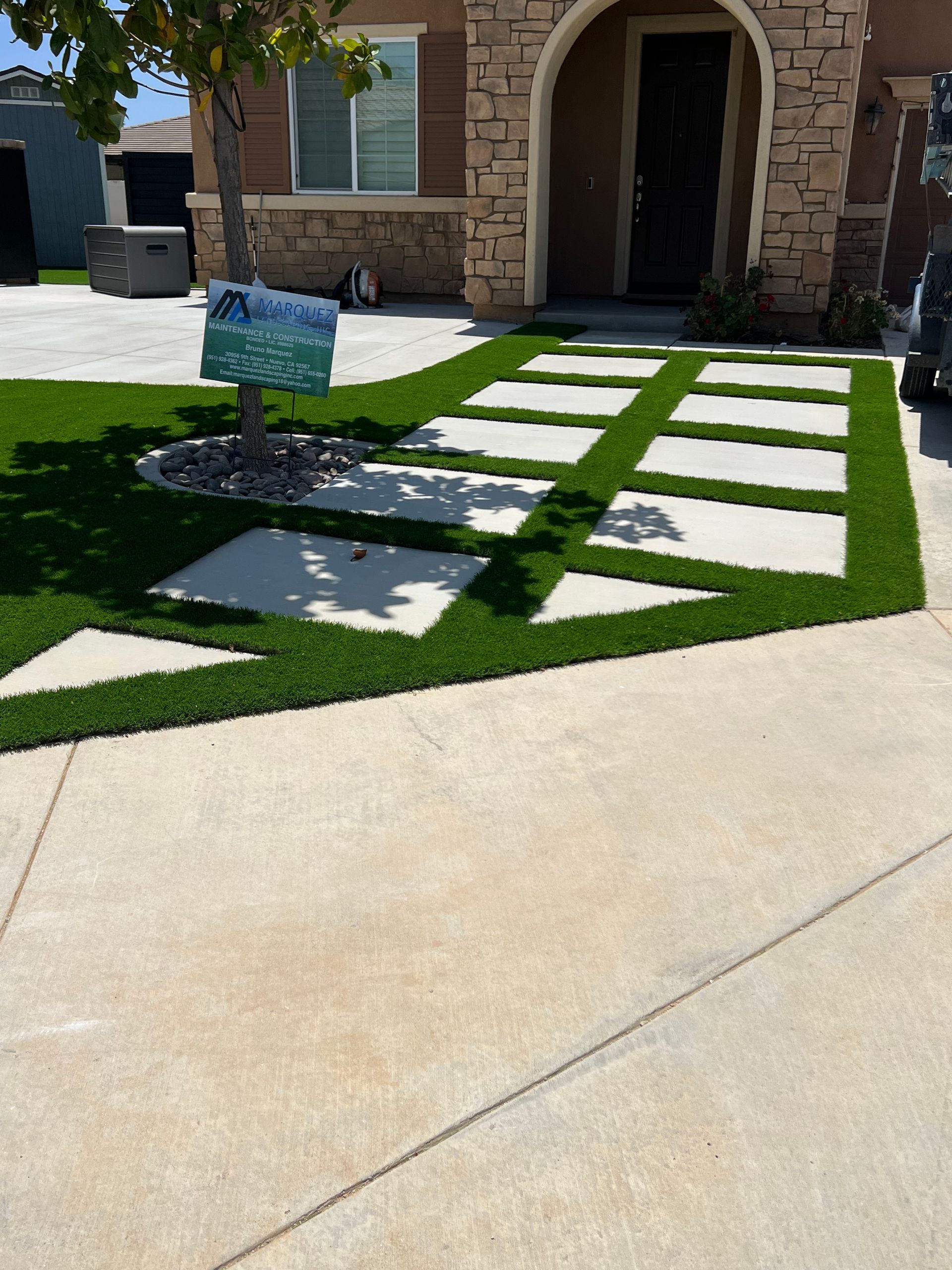Artificial turf and concrete pavers form a walkway to a home's front door with a stone facade.