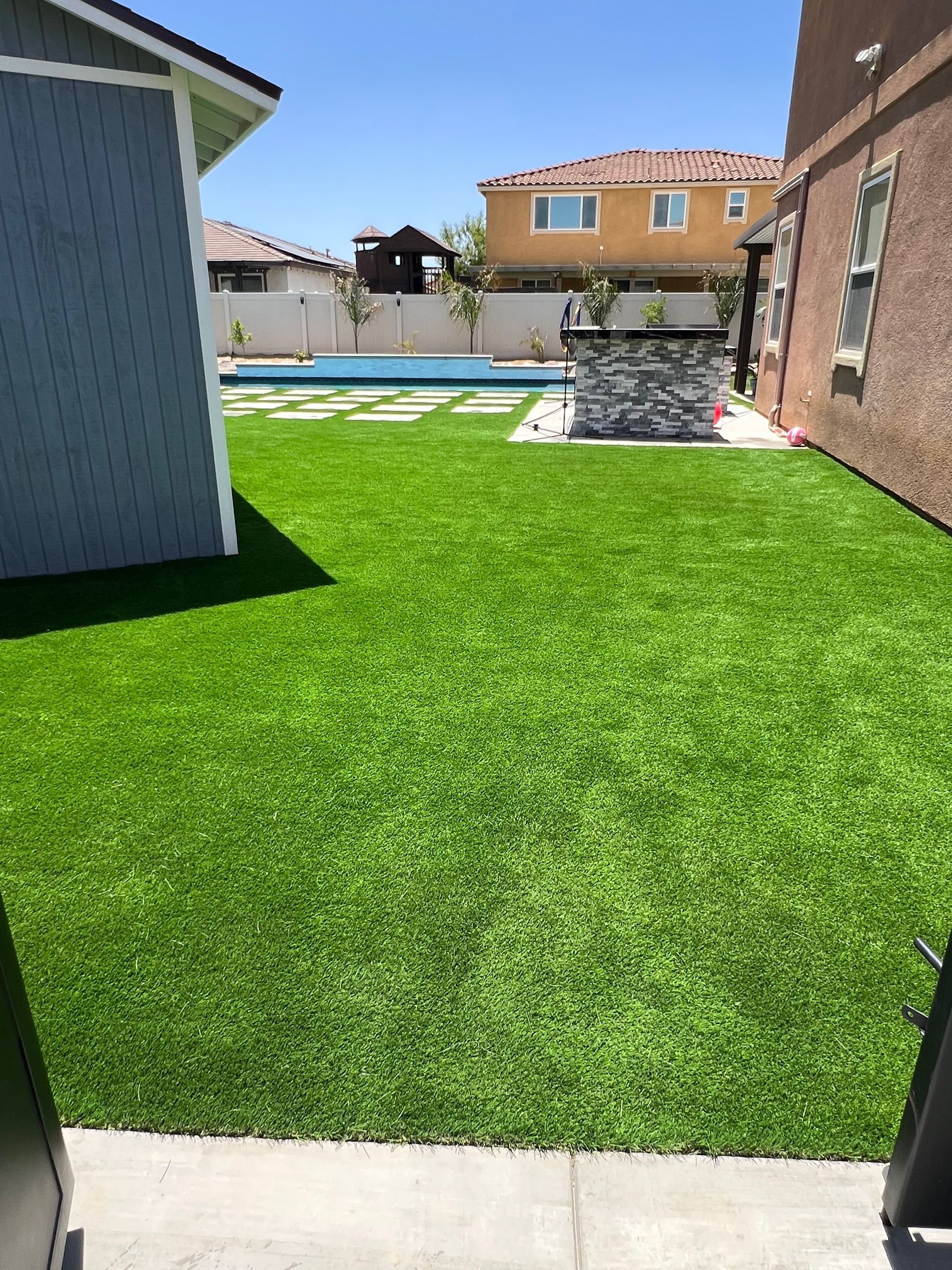 Green artificial grass backyard with a pool and barbecue area.