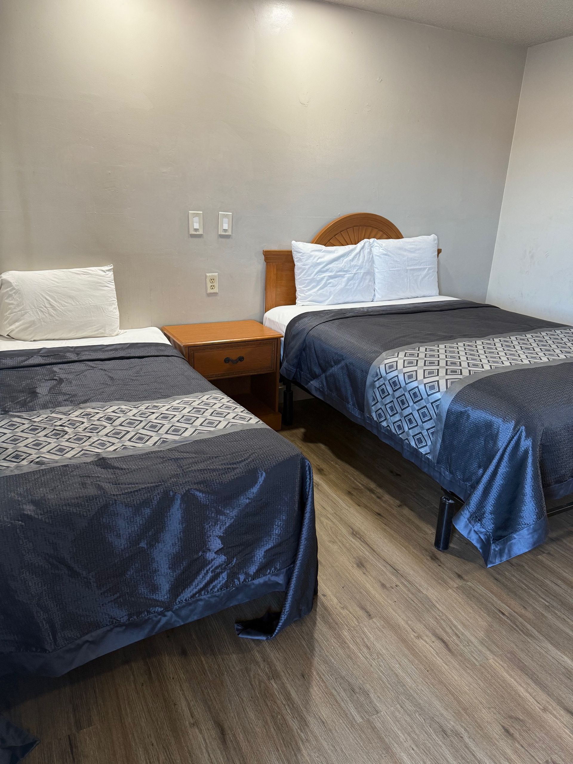 A hotel room with two beds and a nightstand.